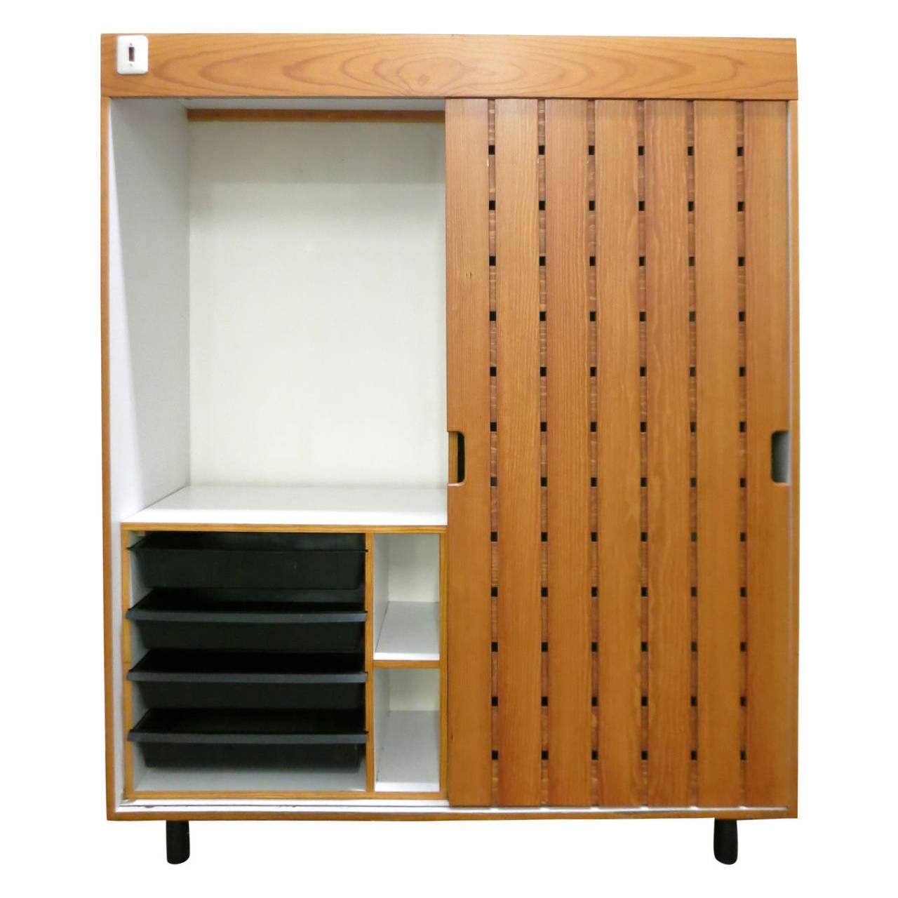 Wardrobe with a single sliding slatted wood door. The interior is white laminate with a separate pull-out cabinet with drawers in molded plastic. Each drawer is stamped 