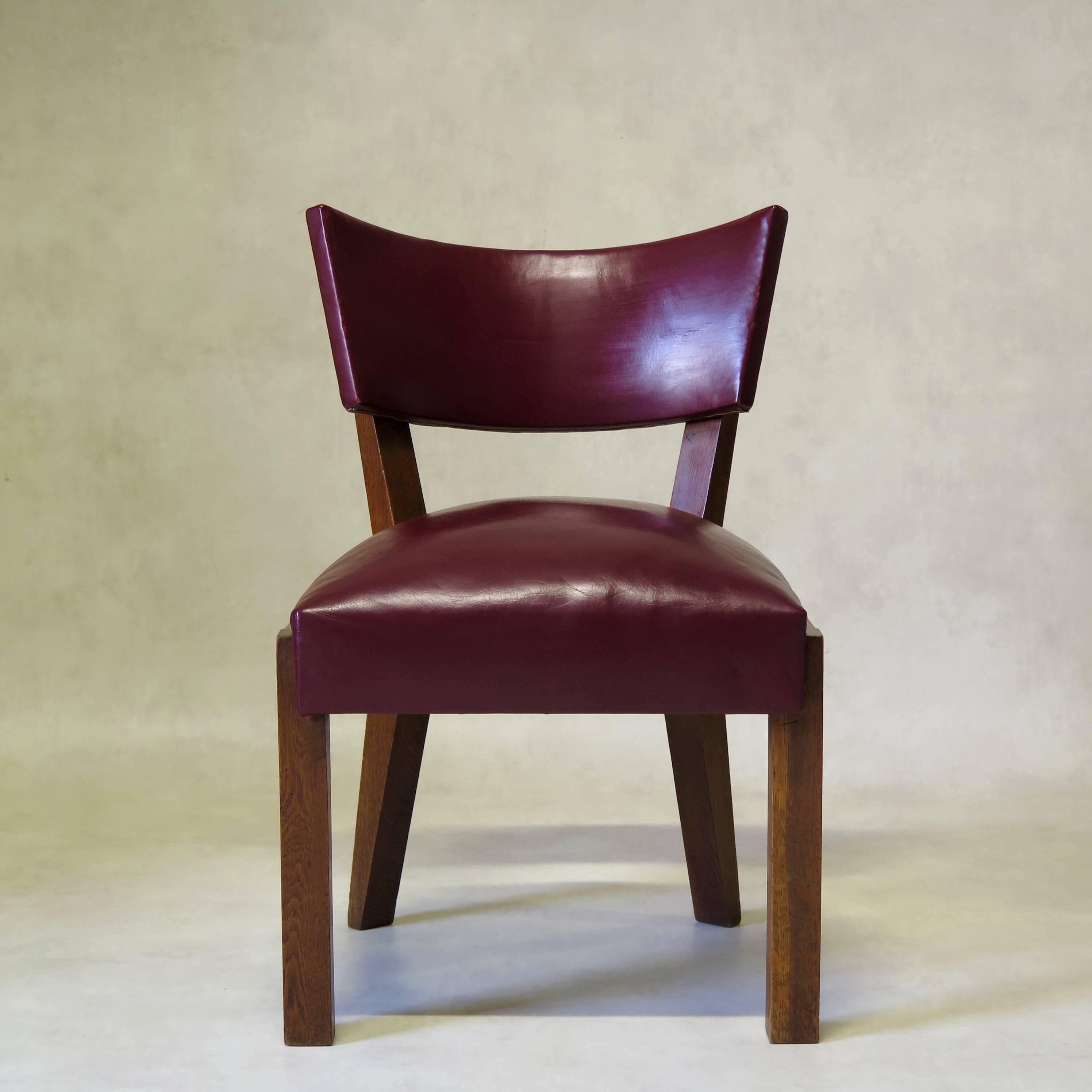Very chic and gorgeous quality set of eight solid oak, 1940s Art Moderne dining chairs of generous proportions, with wide, comfortable seats and curved backs, upholstered in dark red leather, with nailhead trim on the back.
The graphic, unfussy
