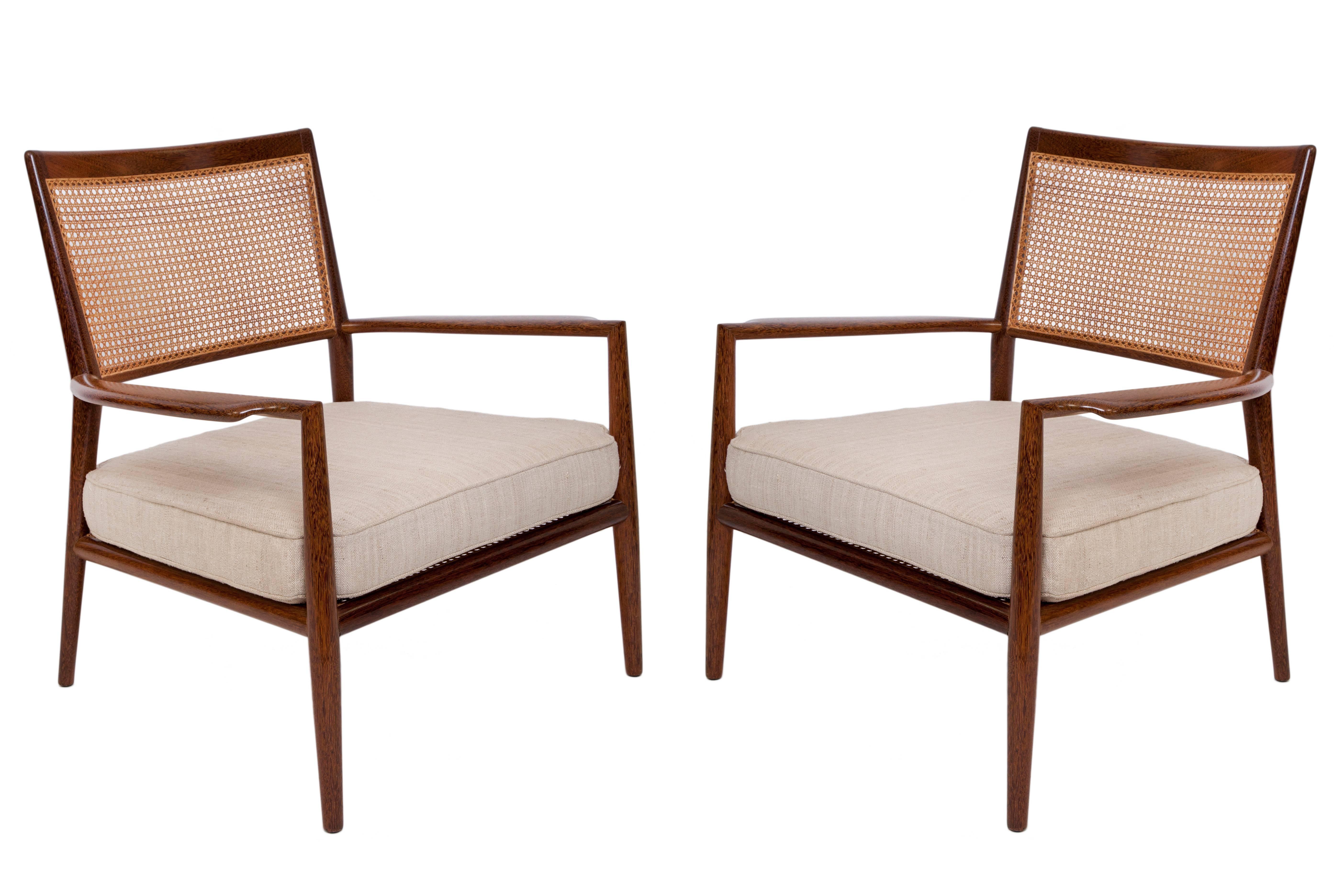 A pair of vintage armchairs, by designer Carlos Milan, produced circa 1960s, framed in sucupira wood with woven cane seat and back, each with upholstered cushion seats in beige linen, on tapered legs. Good condition, with age appropriate wear