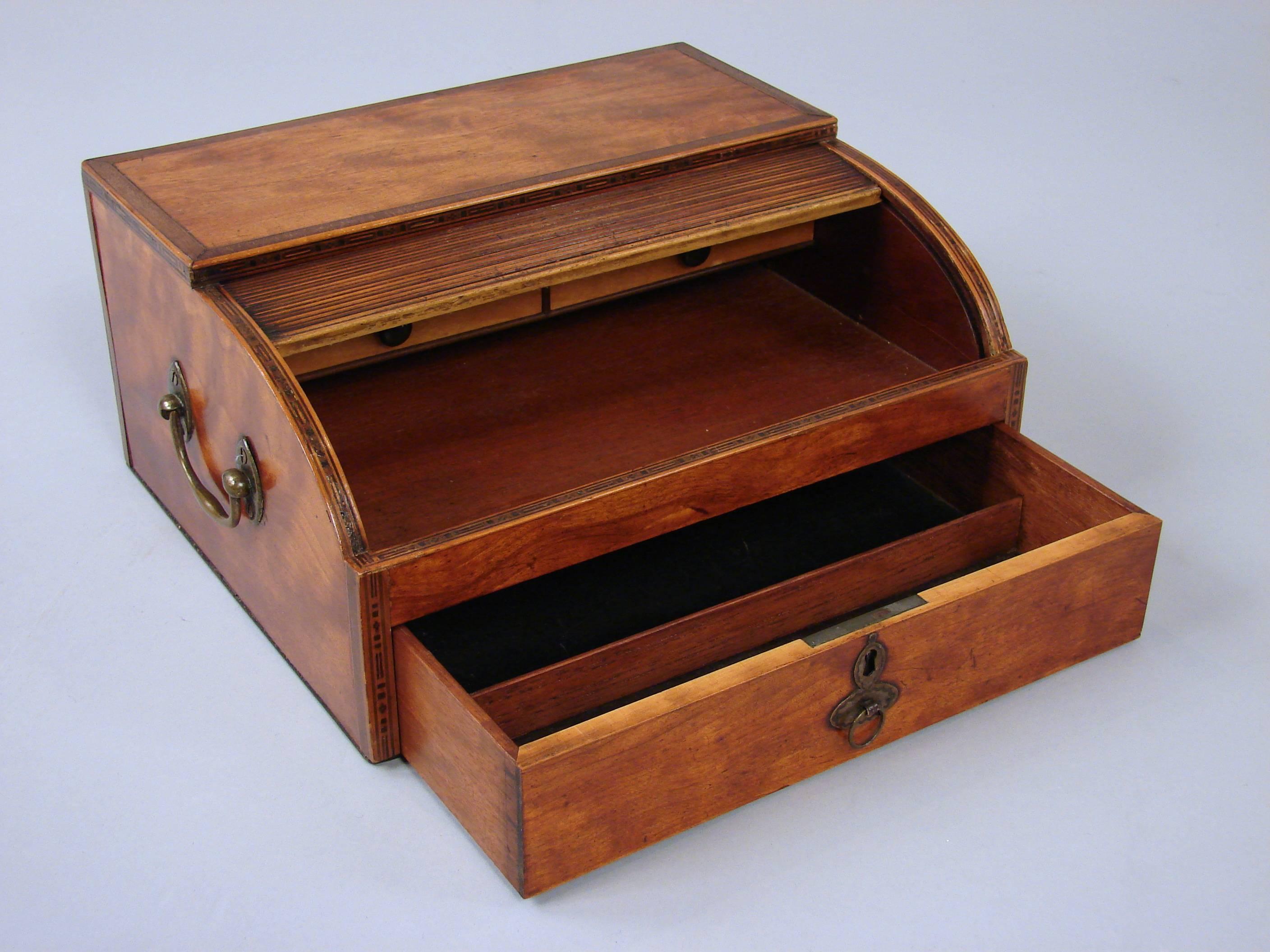 A lovely Georgian satinwood inlaid writing box, the tambour door enclosing a set of drawers with a drawer below, the sides with handles. Opening the tambour causes the drawer to open as well.