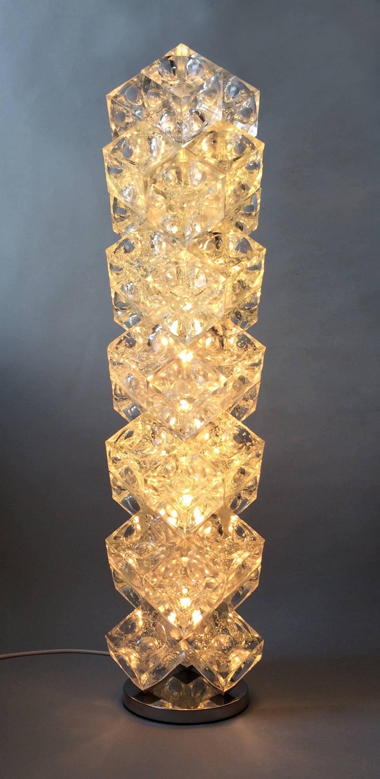 Composition including 36-cube unrefined glass component parts with an internal hemispheric groove and a stainless steel base. The light is divided into seven sections with six internal light bulbs.
