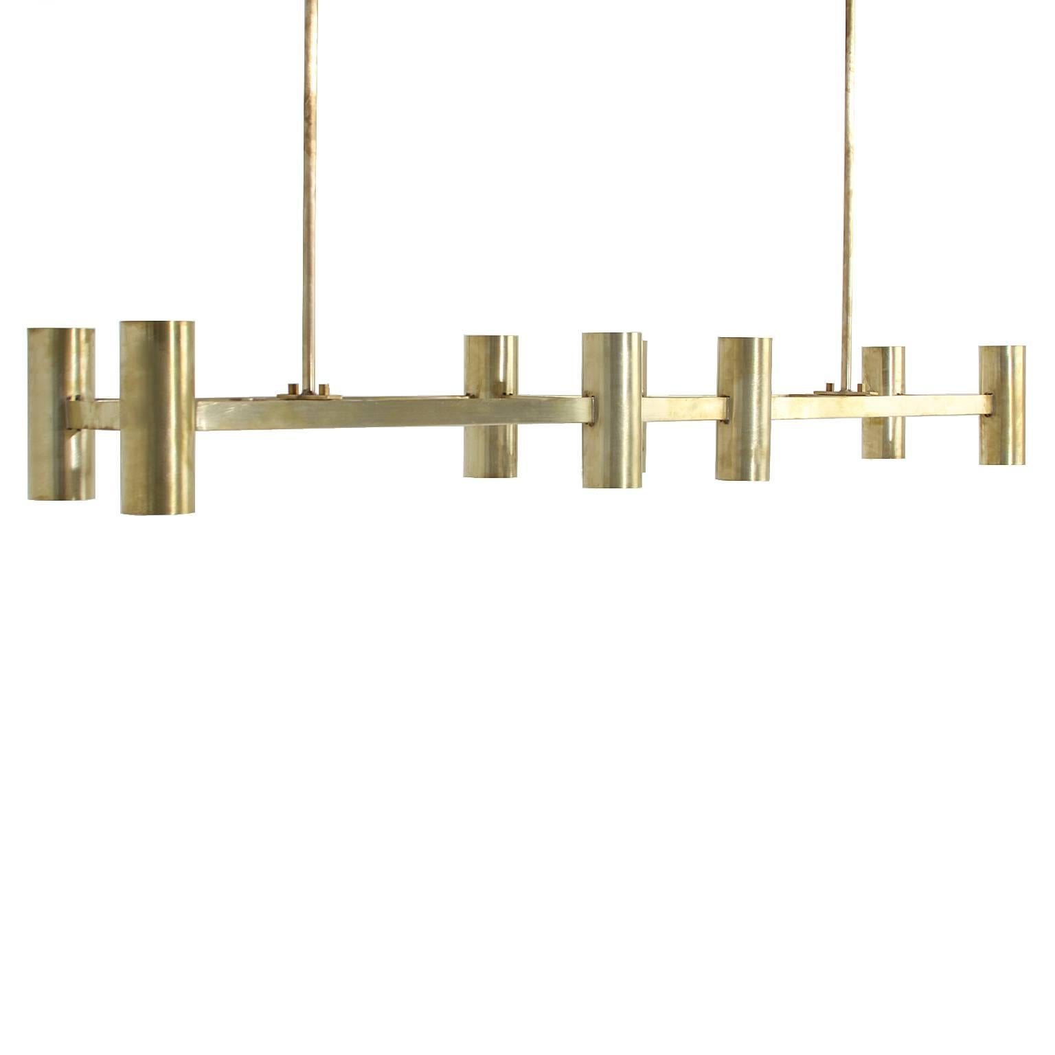 A large chandelier by Thomas Hayes Studio with 8 cylinders on a rectangular support in brushed finish in solid brass. The cylinders have both up lights and down lights, and the light makes the inside of the cylinders appear gold colored when lit.