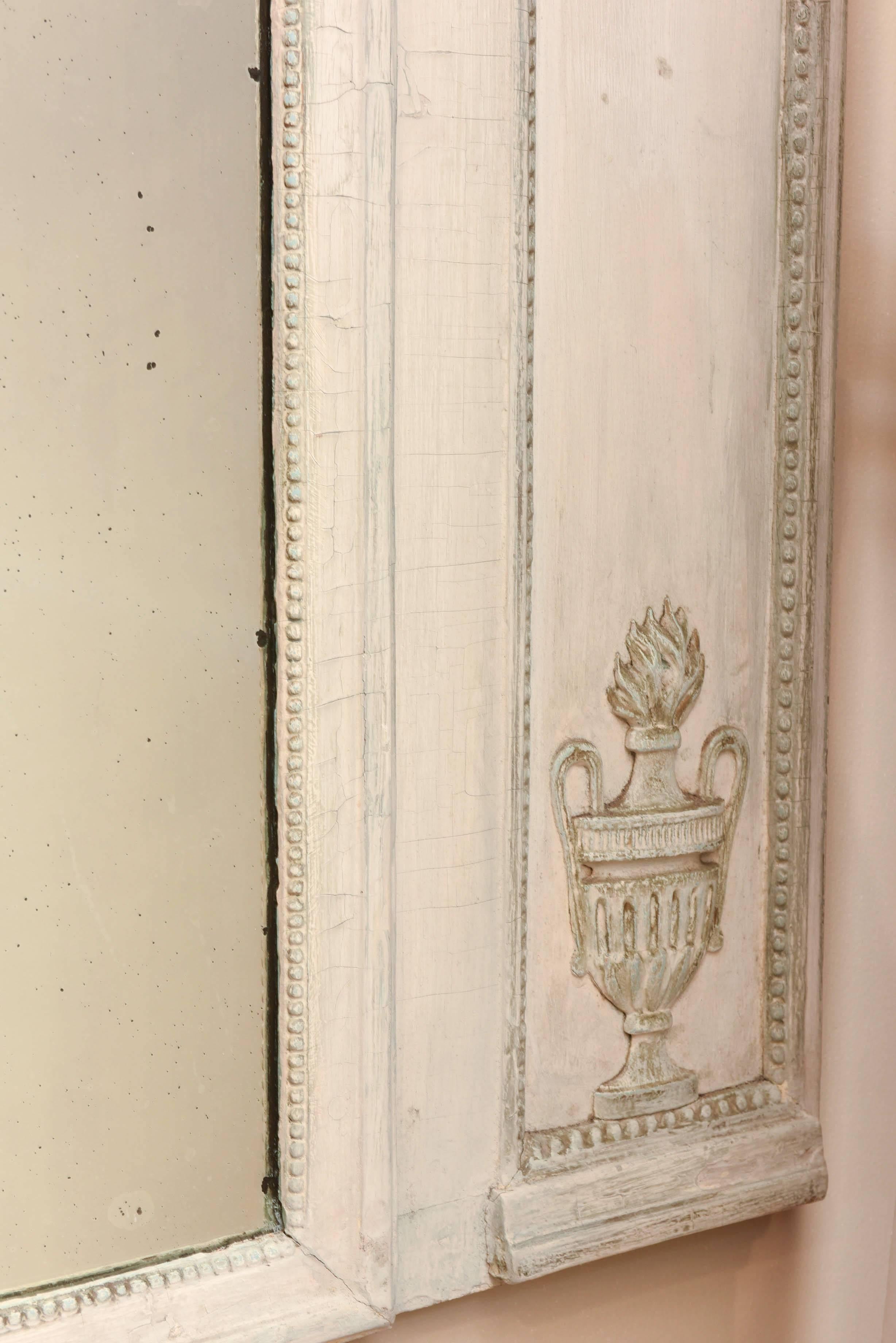 Trumeau mirror, having distressed painted finish, outcarved floral and urn motifs on side panels, centered with exquisitely carved raised basket of flowers separating two antique, spotted, diamond dust mirror panels, surmounted by molded cornice.