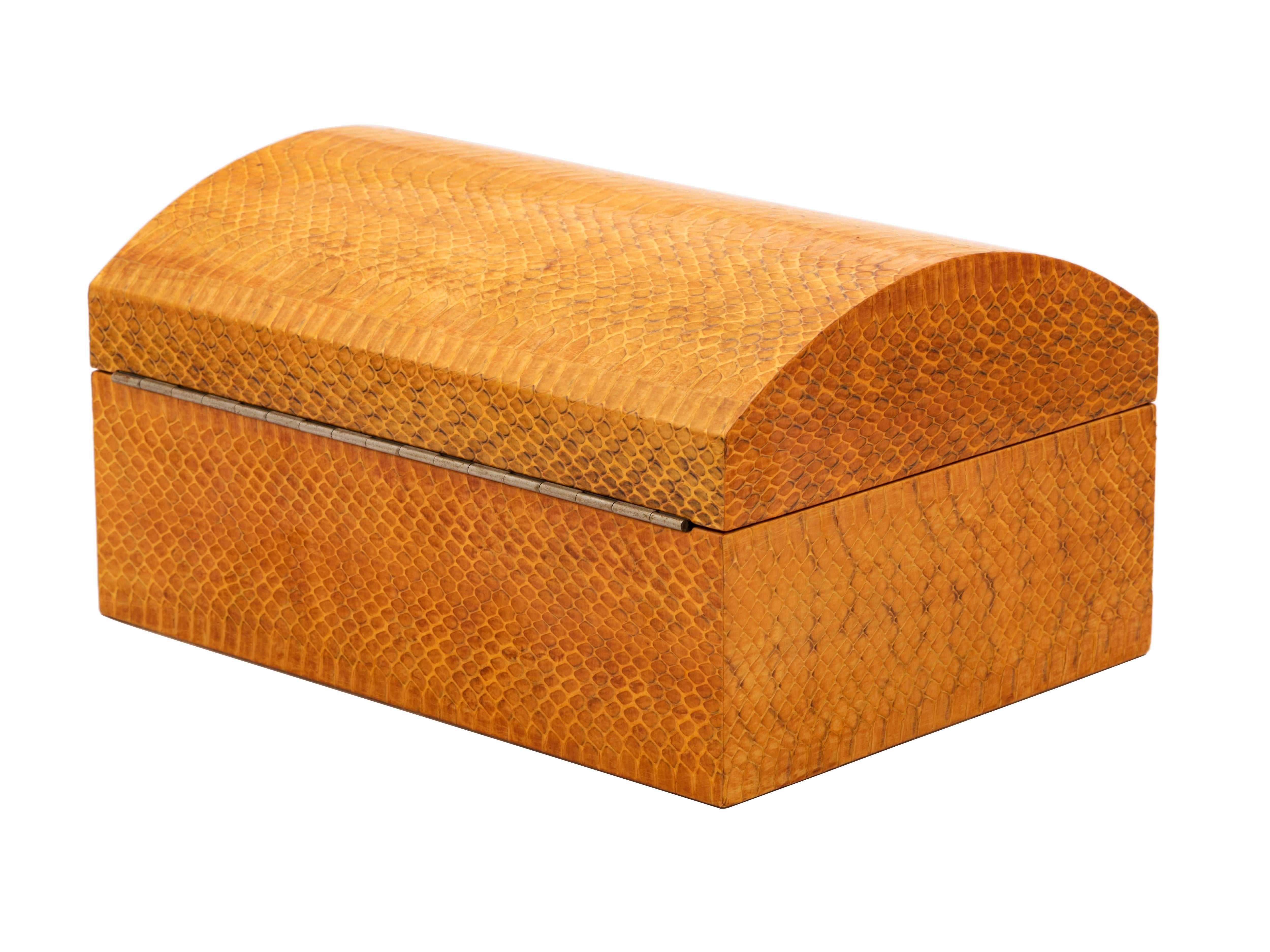 A scrupulously-crafted, decorative trinket or jewelry box by Karl Springer comprising a rectangular body with a domed, hinged lid and a suede-lined interior. The outside is wrapped entirely in lacquered snakeskin in a rich, warm honey color with
