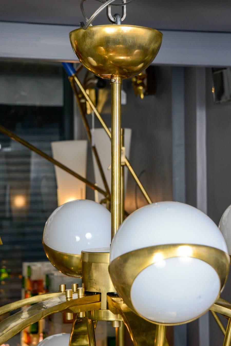 Original brass circular chandelier made of six arcs each supporting four lights set in white glass globes.