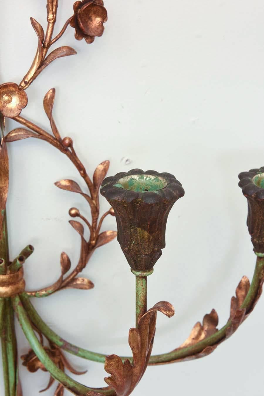 Pair of sconces, painted and parcel-gilt iron, with each backplate formed as an arrow, embellished by curling vines, surmounted by a ribbon bow, four foliate-decorated C-scroll candle arms, ending in scalloped candle pots. Not electrified.

Stock