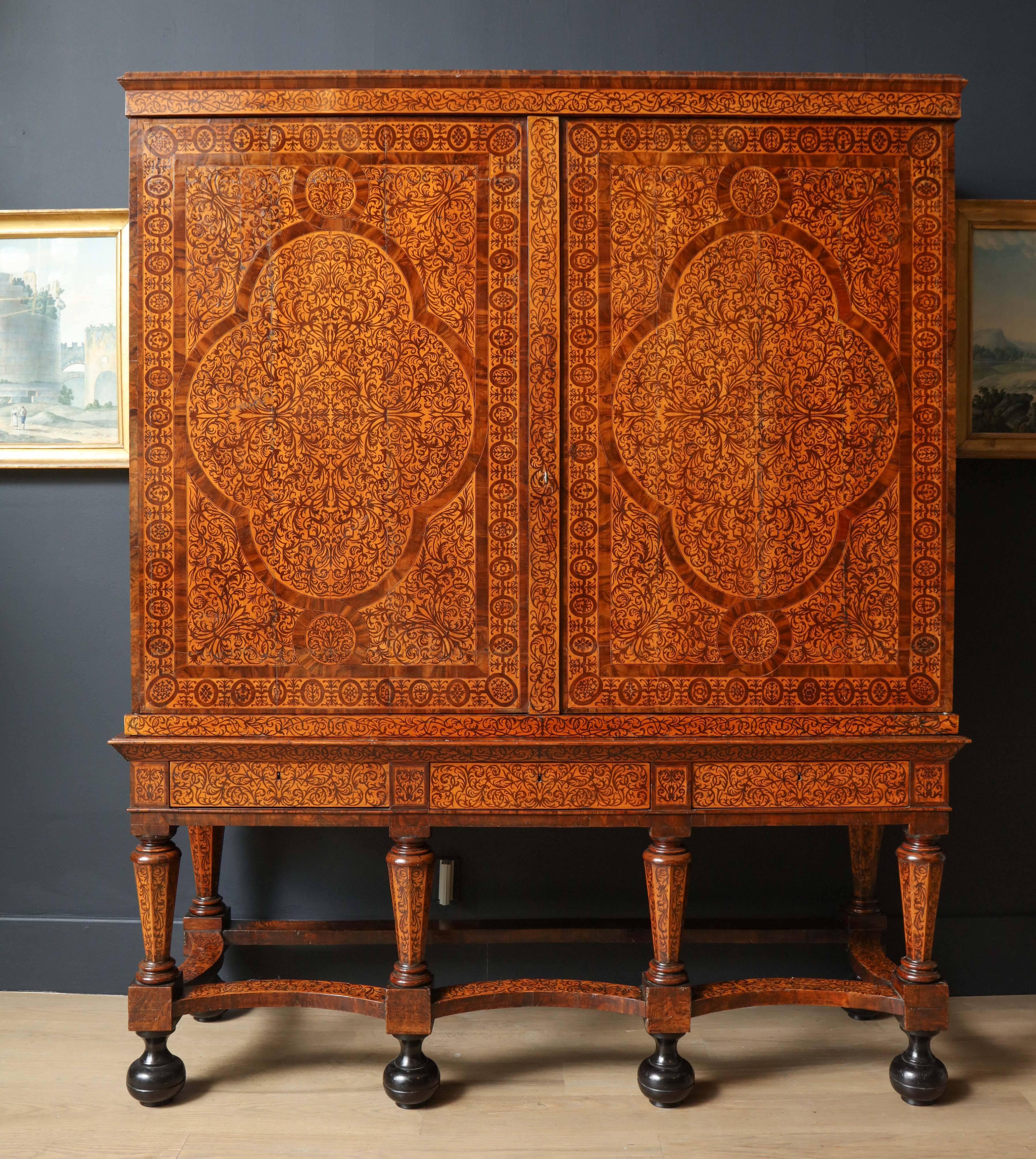 Inlaid throughout with intricate scroll patterns with large decorative cartouches on all sides of the cabinet with flat cornice raised on a stand of octagonal tapering legs and ebonized bun feet. Fitted with drawers and shelves inside.

Produced
