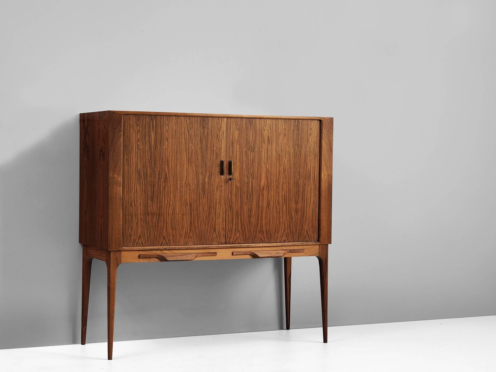 Dry bar, in rosewood and glass, by Kurt Østervig, Denmark, 1960s. 

Real exclusive Danish liquor cabinet. Designed on high legs for easy access and two shelfs that slide out front to prepare the best cocktail imaginable. The tambour sliding doors