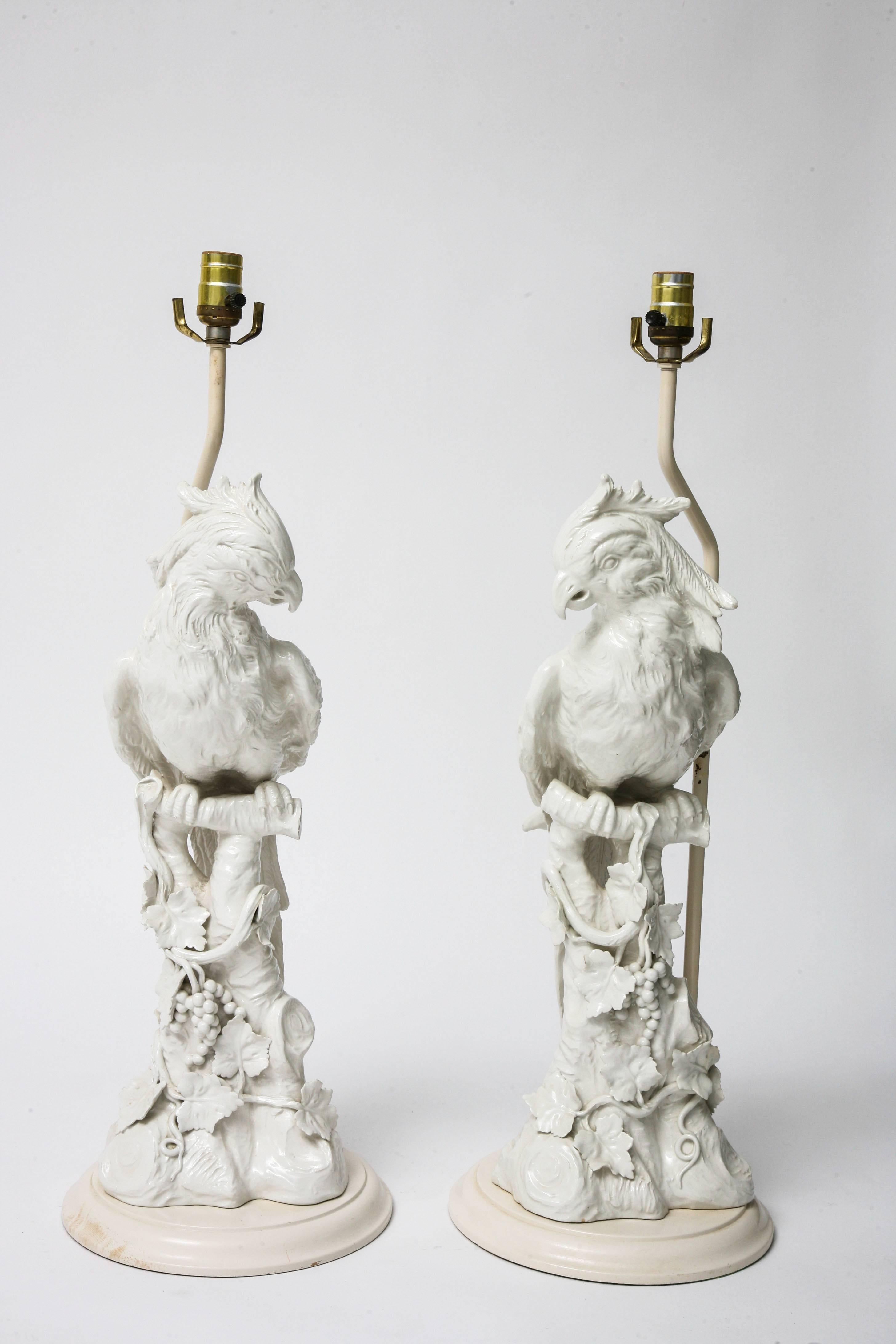 This pair of table lamps are the height of the Hollywood-Regency Style from the mid-part of the century. The figural parrots are (Italian) ceramic with a bone-white glaze and the base is a light-beige-white coloration. 

Note: The dimensions of
