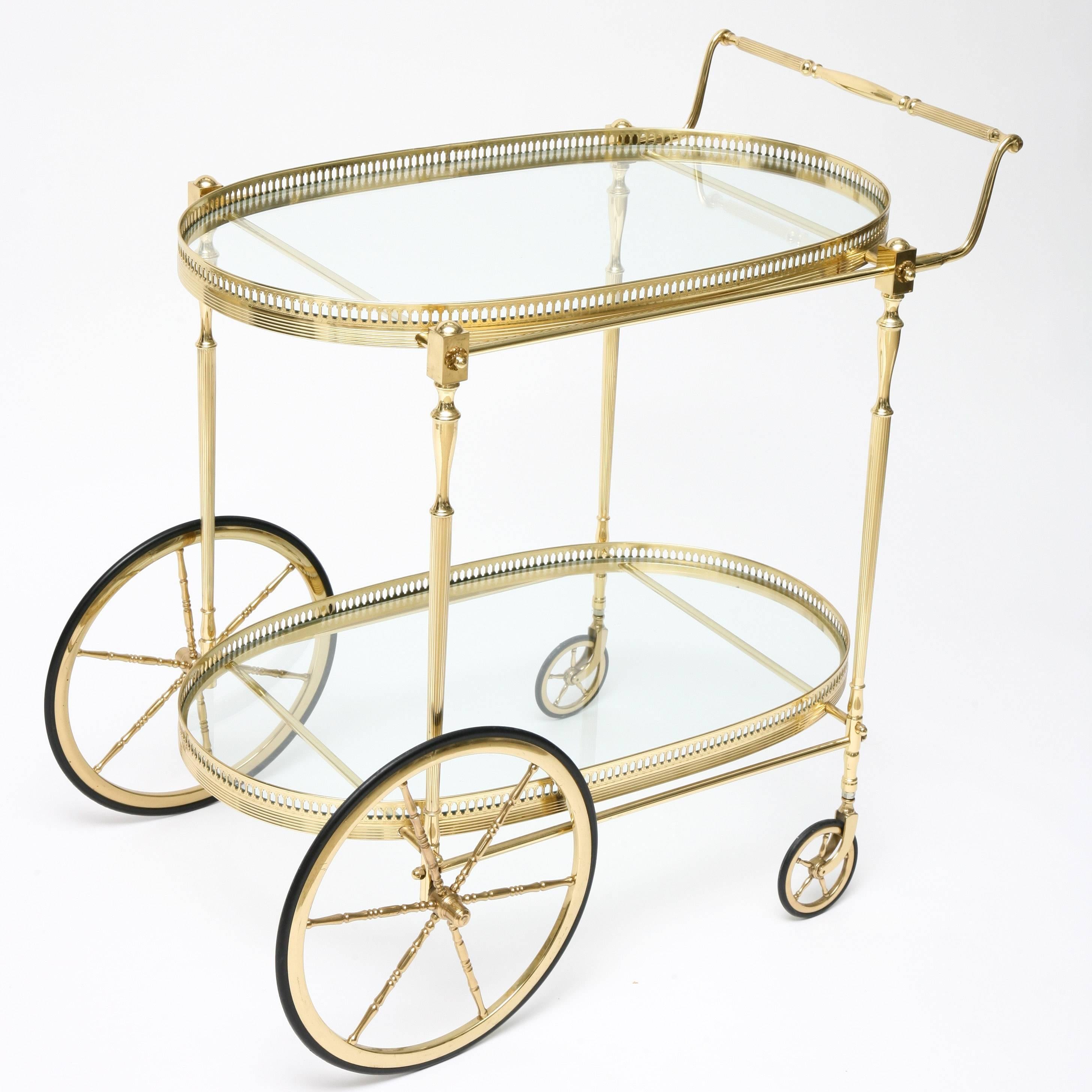 This glamorous Hollywood-Regency style polished brass and glass, two-tiered, race-track design bar cart is very much in the style and quality of pieces created by Maison Jansen in the 1960s and 1970s. With its tray-like upper and lower sections