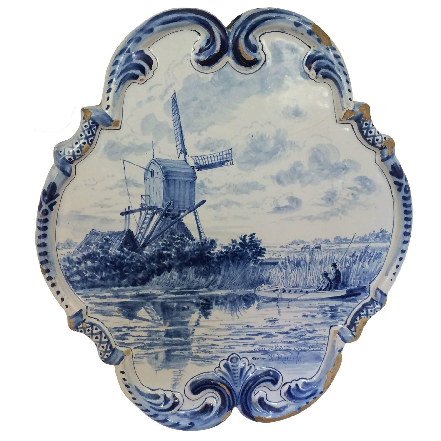 Blue and white delft wall plaque; two men in a boat fishing in a lake with cattail border; windmill in the background; beautifully detailed raised border; 18th century.