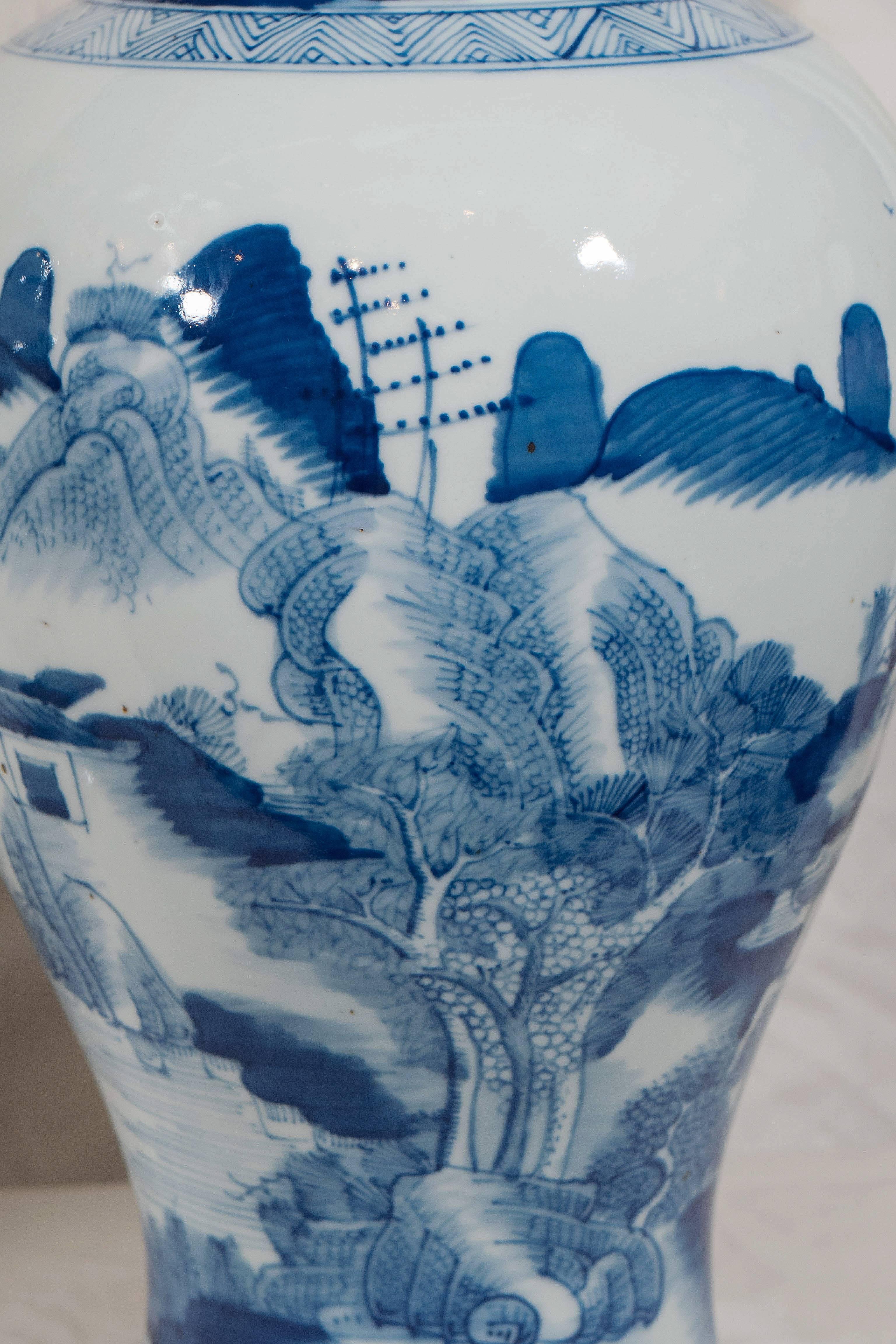 A pair of blue and white Chinese porcelain covered jars with graceful proportions hand painted in timeless cobalt blue. The jars are decorated with pagodas and mountainside scenes reaching up to the sky. The overall effect is serene. The covers have