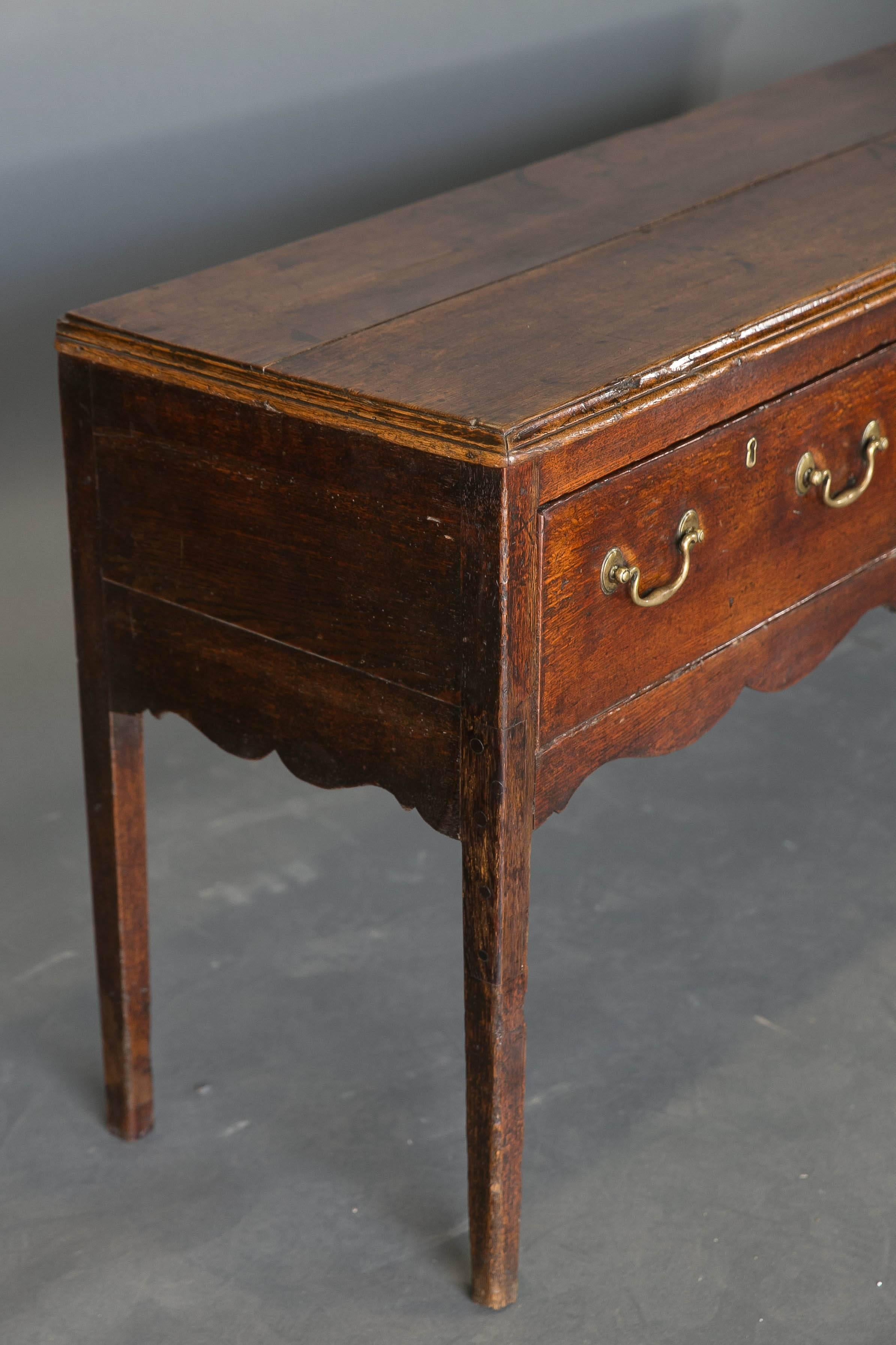 19th century oak dresser base with scalloped apron. The piece has three drawers with swan neck brass hardware and sits on tapered legs. Good color and beautiful patina.
