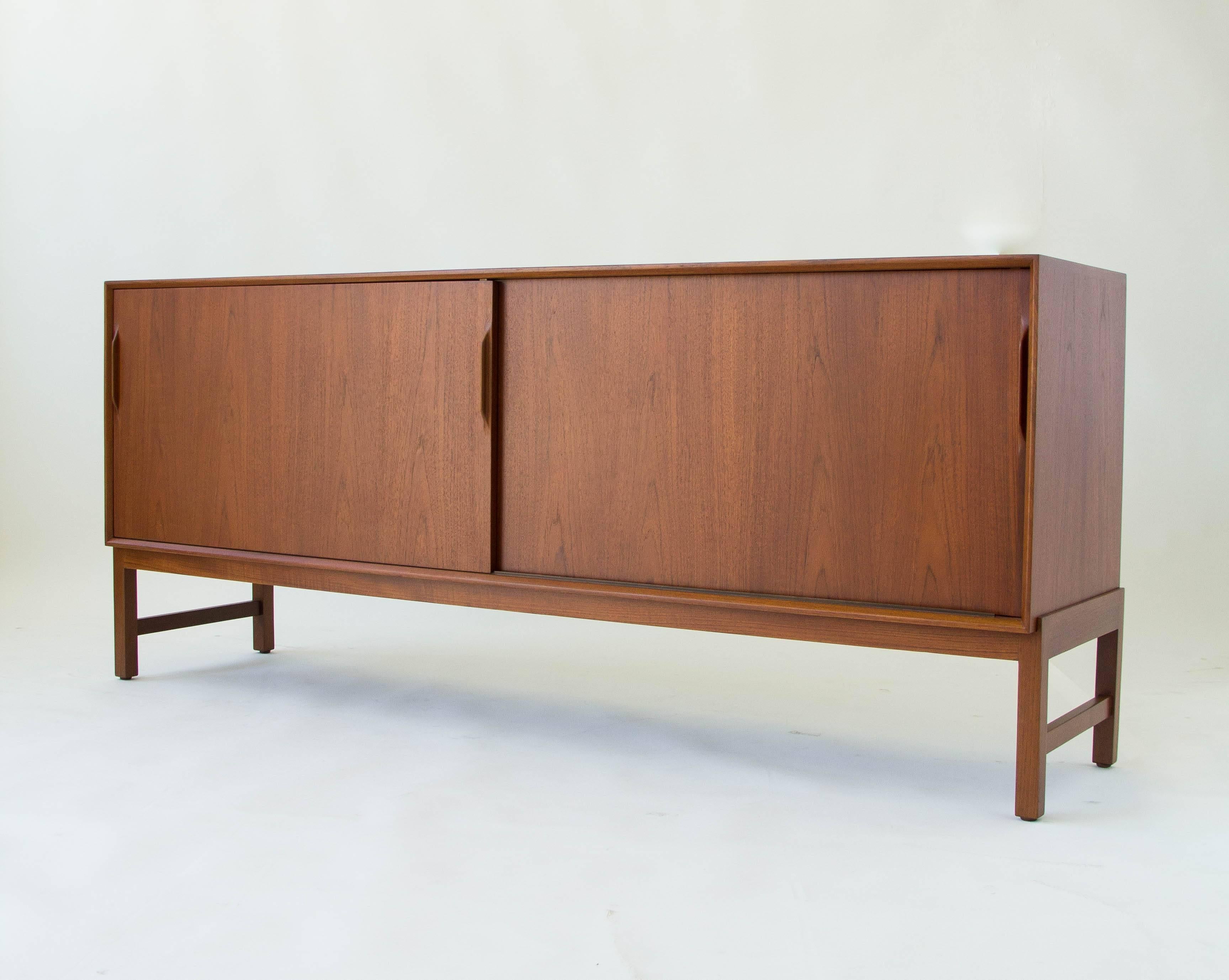 Three-compartment teak credenza by Karl-Erik Ekselius for JO Carlsson of Sweden. Solid teak legs sit flush with the case. The interior storage, accessible by two sliding doors, has modular dovetail drawers to accommodate a variety of storage
