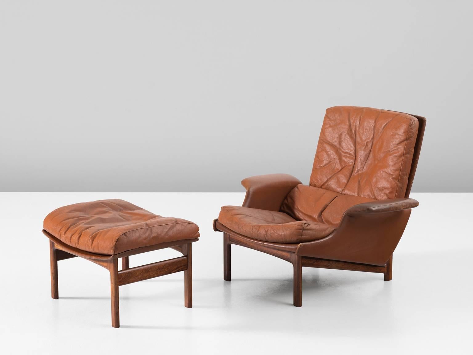 Adam lounge chair, in leather and teak by Ib Kofod-Larsen for Mogens Kold Møbelfabrik, Denmark, 1958. 

Extraordinary lounge chair accompanied by an ottoman. Rare to find as a pair. This very comfortable high back chair comes with characteristic