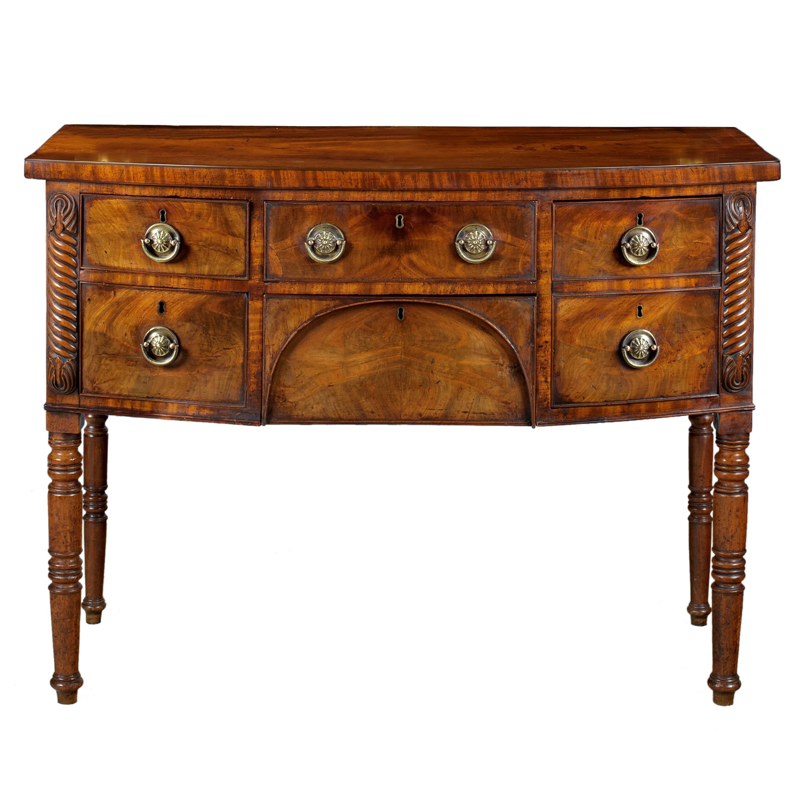 A very pretty and small Regency period mahogany bow fronted sideboard with a two drawers to the left, a drawer and an arched napery drawer to the centre and a deep drawer to the right flanked by stylized palm fronds with a cable or rope twist