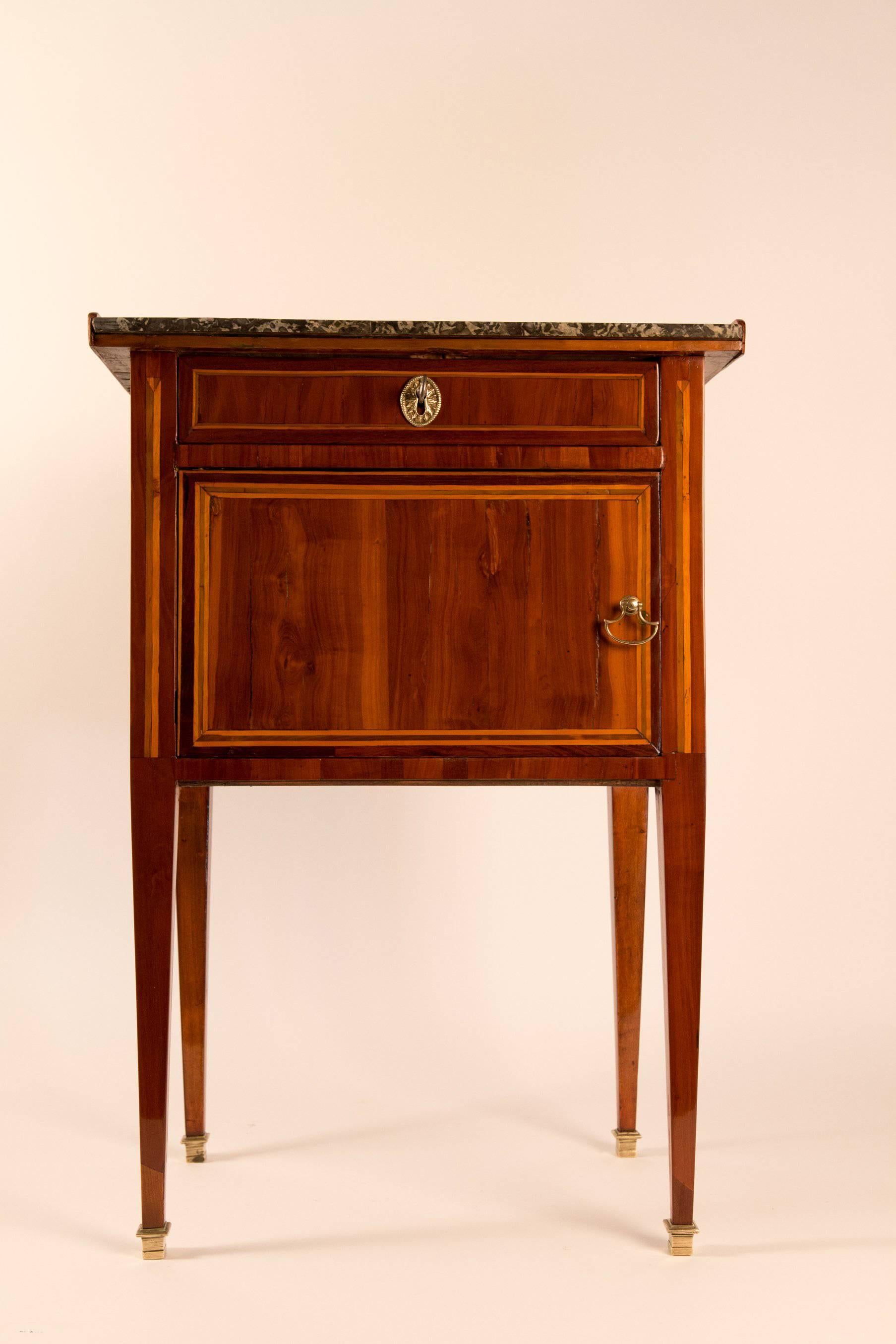 An lovely Louis XVI period, walnut, plumwood, sycamore and boxwood, small commode or small side table. Our side table opening by one drawer and a small door. It rests on elegant “gaine” legs, with a “Grey Sainte-Anne” marble top. Original bronze