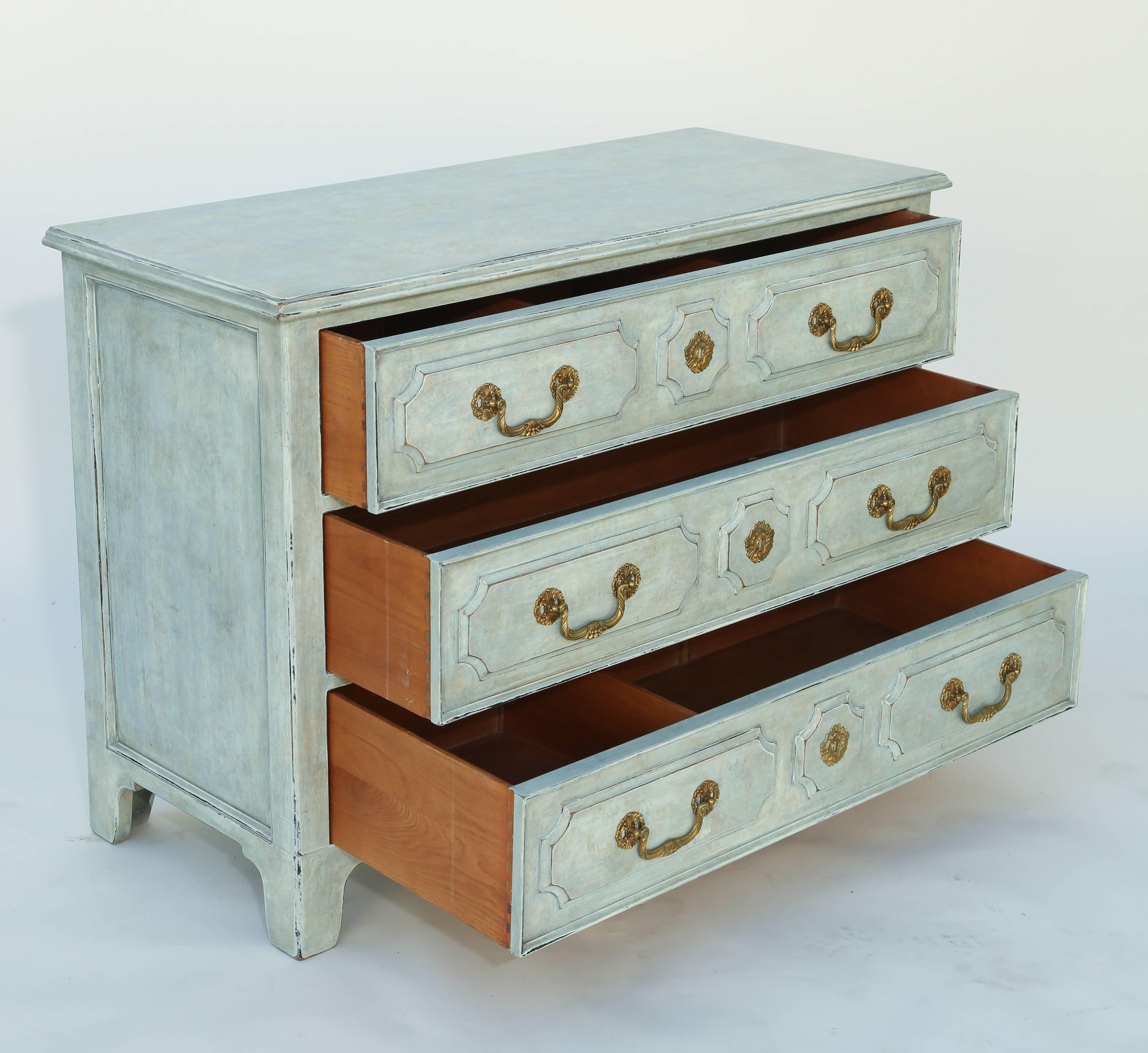Chest of three drawers, having a mottled painted finish in light blue, its molded rectangular top on stacked raised panelled drawers with brass escutcheons and pulls with fielded sides, raised on bracket feet.

Stock ID: D6984