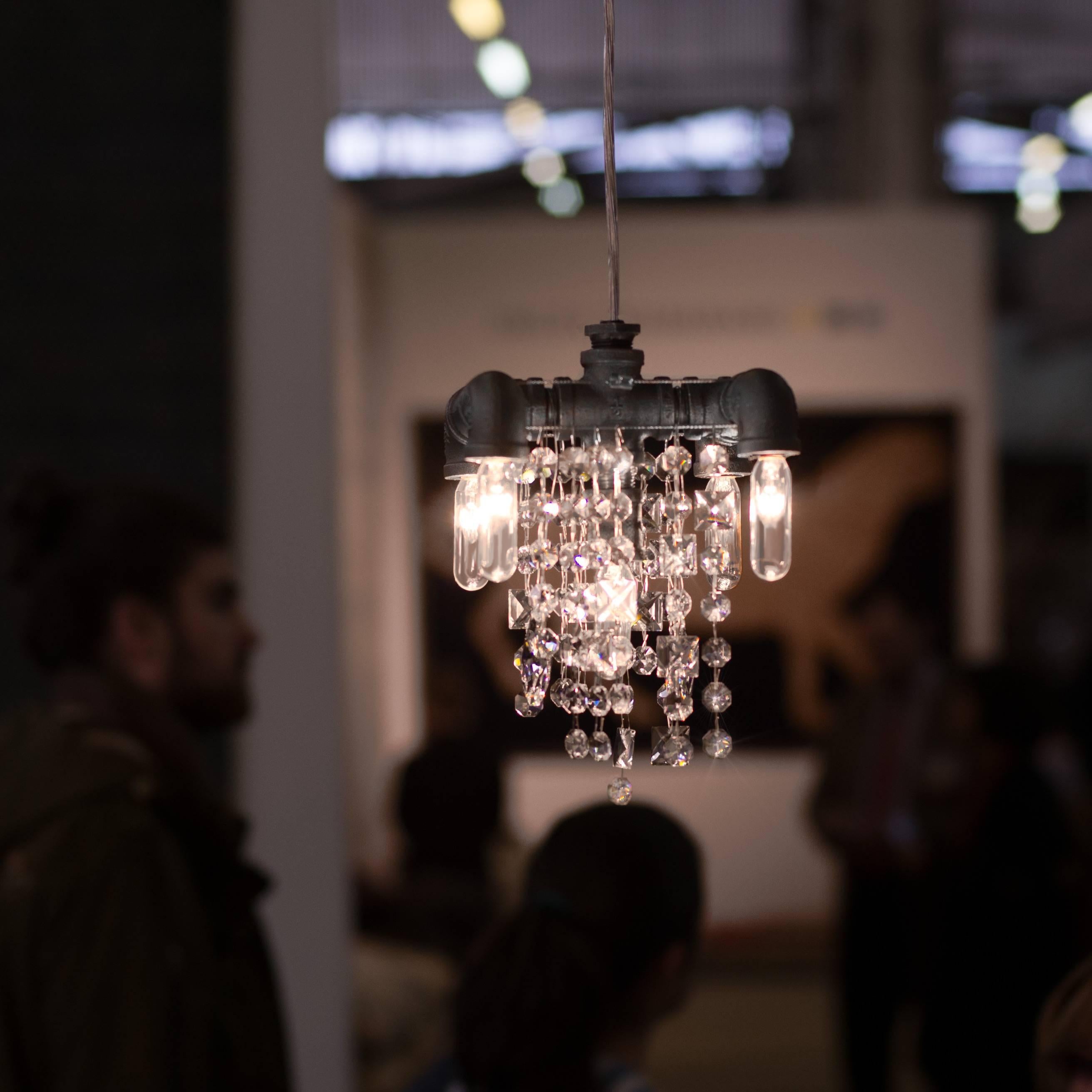 A modern pendant chandelier features a compact Industrial frame with five lights on two levels which is paired with superior quality optically pure crystal in a random array which suggests falling water.

Though only measuring 6.5 Width x 6.5