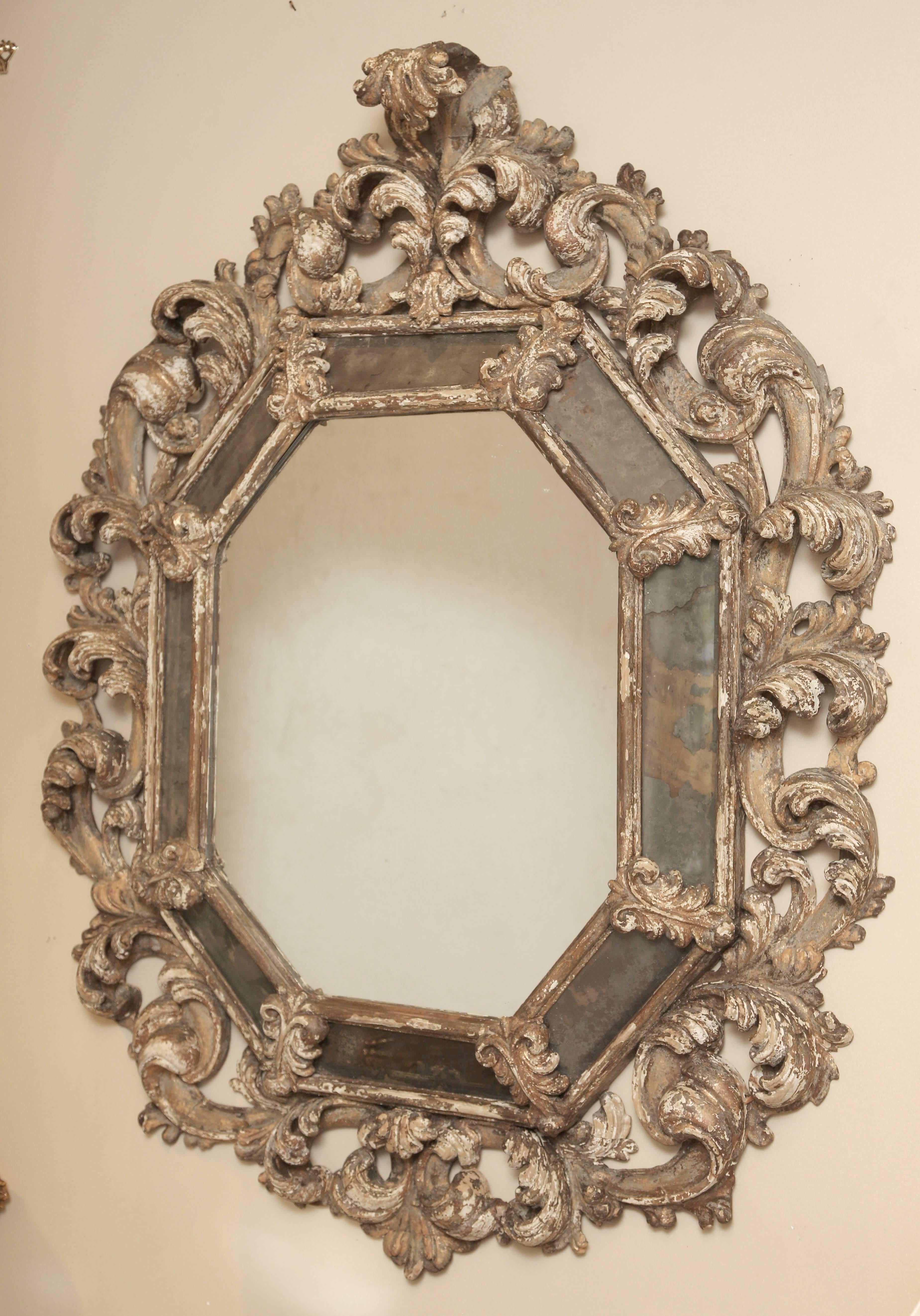Mirror, of distressed painted and gessoed wood, having an octagonal mirror plate, bordered by original antique mirrored reliefs, surrounded by elaborately carved pierced foliate frame.

Stock ID: D3704