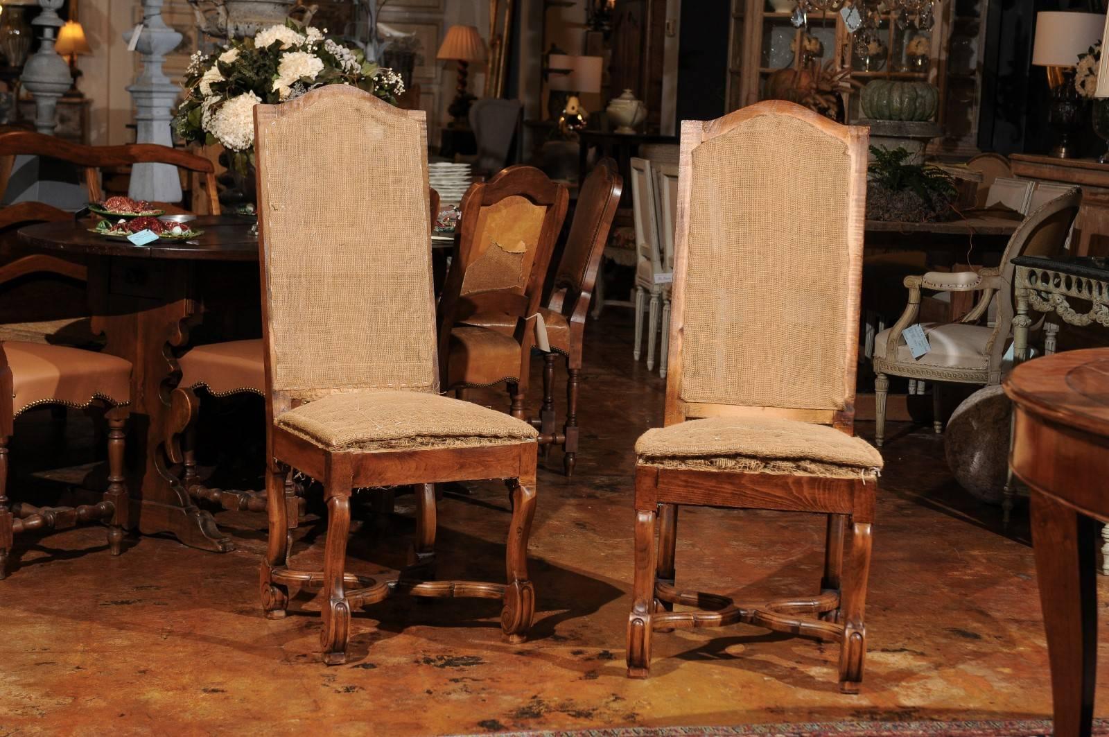 This set of six French Louis XIII style walnut os de mouton side chairs from the early 20th century features tall slightly slanted backs over simple skirts. The rather simple, unpretentious shape of the upper section is covered in burlap and is