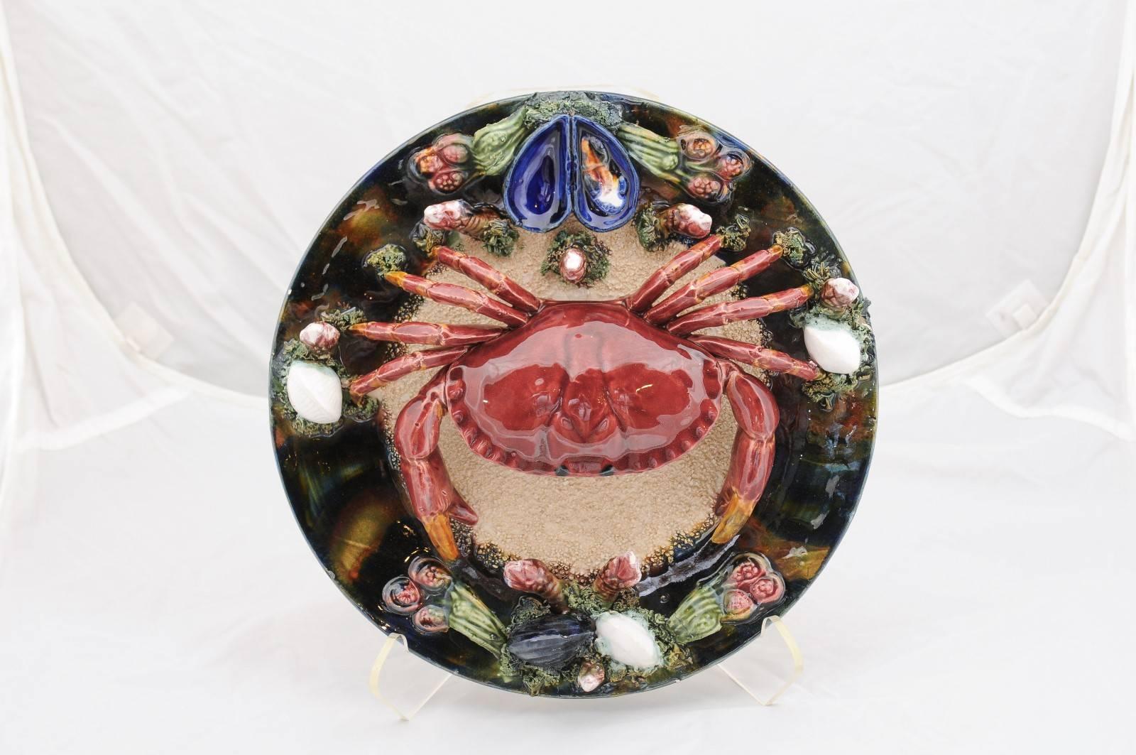 A Portuguese majolica Palissy style small crab plate glazed with vivid colors from the mid 20th century. This Portuguese majolica plate features a hyper-realistic high-relief crab occupying the center of the plate, surrounded by motifs of the sea