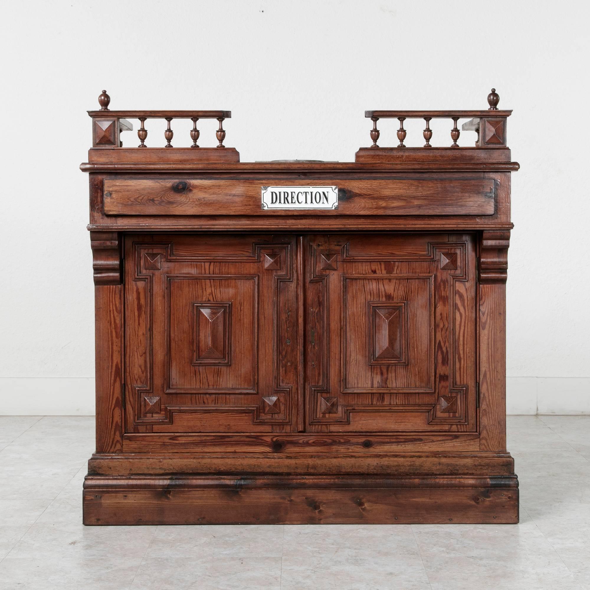Originally in a French shop, this pitch pine counter features a spooled gallery at the top with diamond pointed corners topped by finials. A metal plate on the top toward the front of the counter was used to lay down coins and count back change. The