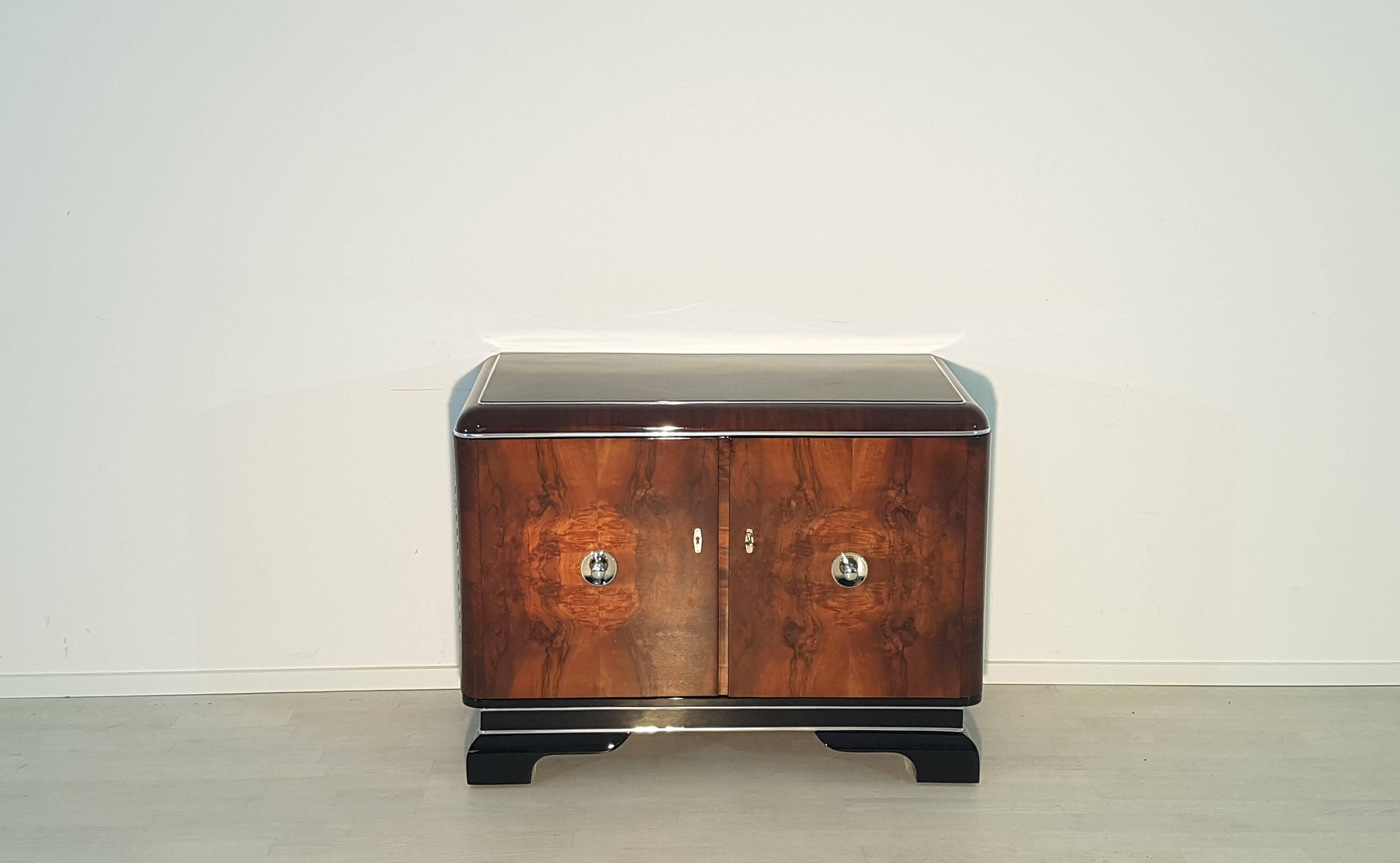 Wonderful Art Deco commode or small dresser with walnut doors and luxurious chrome handles. This unique original piece from the 1920s convinces with its typical Art Deco design and with the great combination of black high gloss lacquer and luxurious