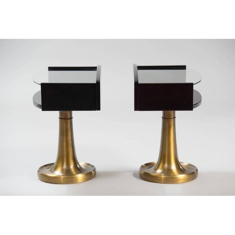 A pair of black lacquered wood and glass nightstands on a brass pedestal.