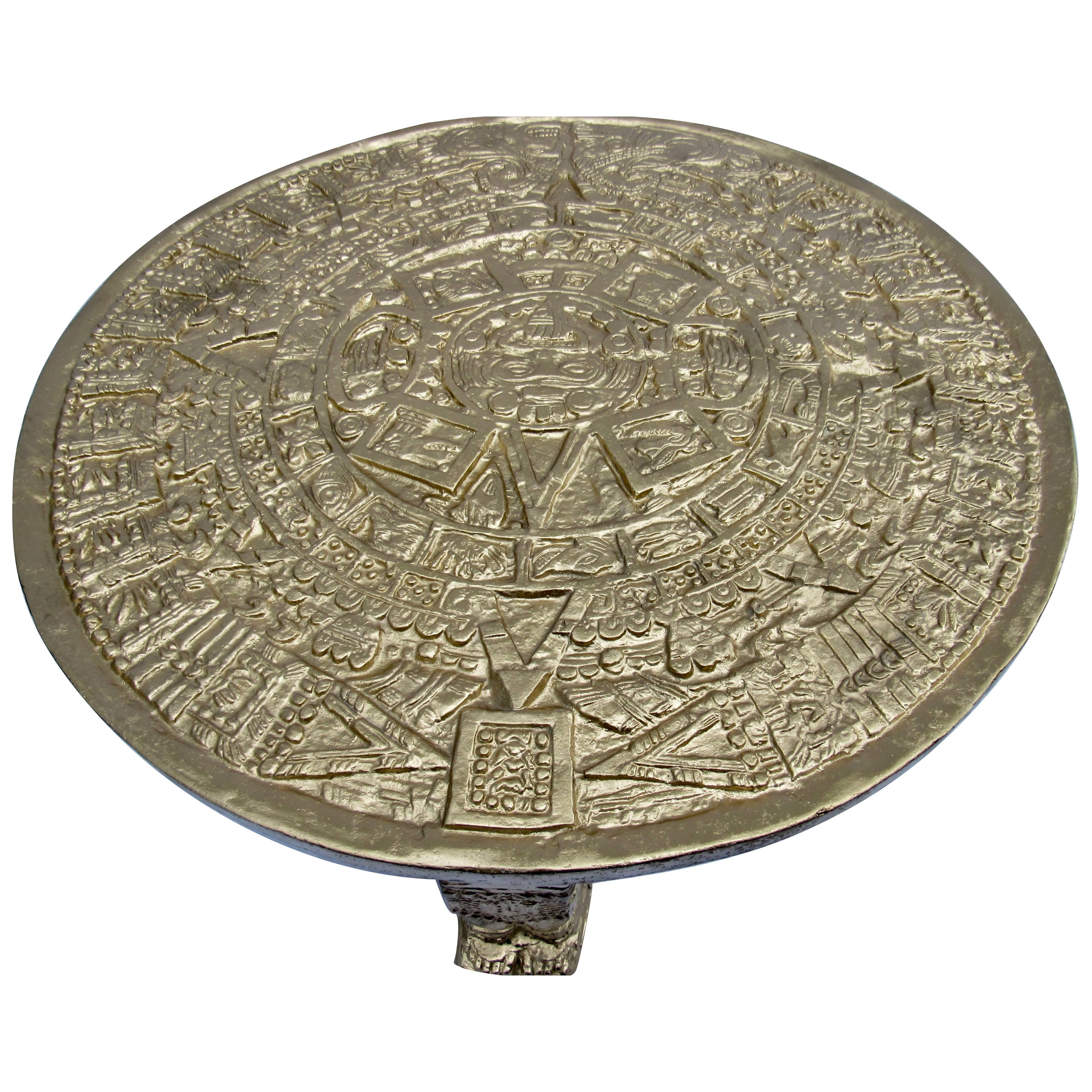 A 1960s Mexican gilded cast aluminum Aztec calendar rests on three cast Aztec sarcophagus figures. The table base weighs 65 lb.s. and is a modernist interpretation of the Pre-Columbian Classic Aztec stone calendar. 
The table measures 110 cm. by 40