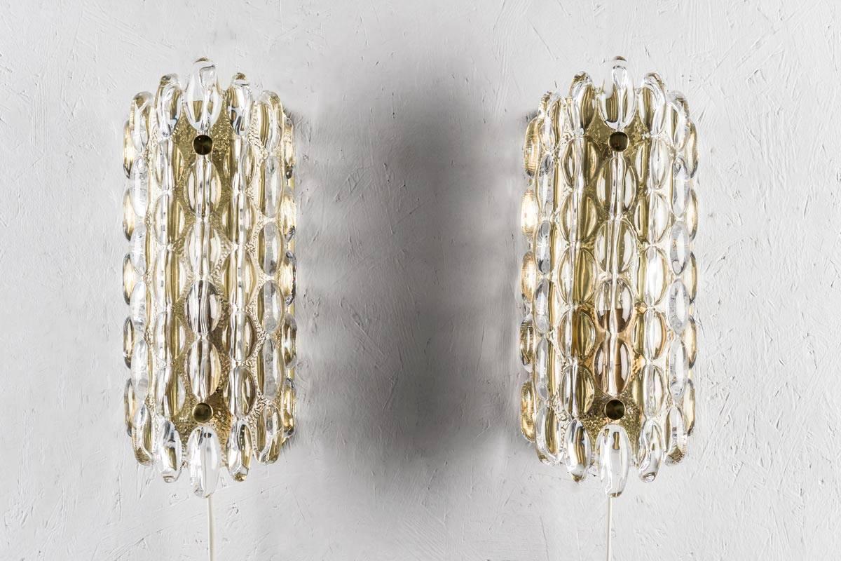 Beautiful wall lamps by Carl Fagerlund for Orrefors, Sweden. The lamps consist of a crystal glass block fixtured on a brass bottom. The glass consist of glass water drop shapes and spreads a beautiful pattern when lit up. 
Four pieces