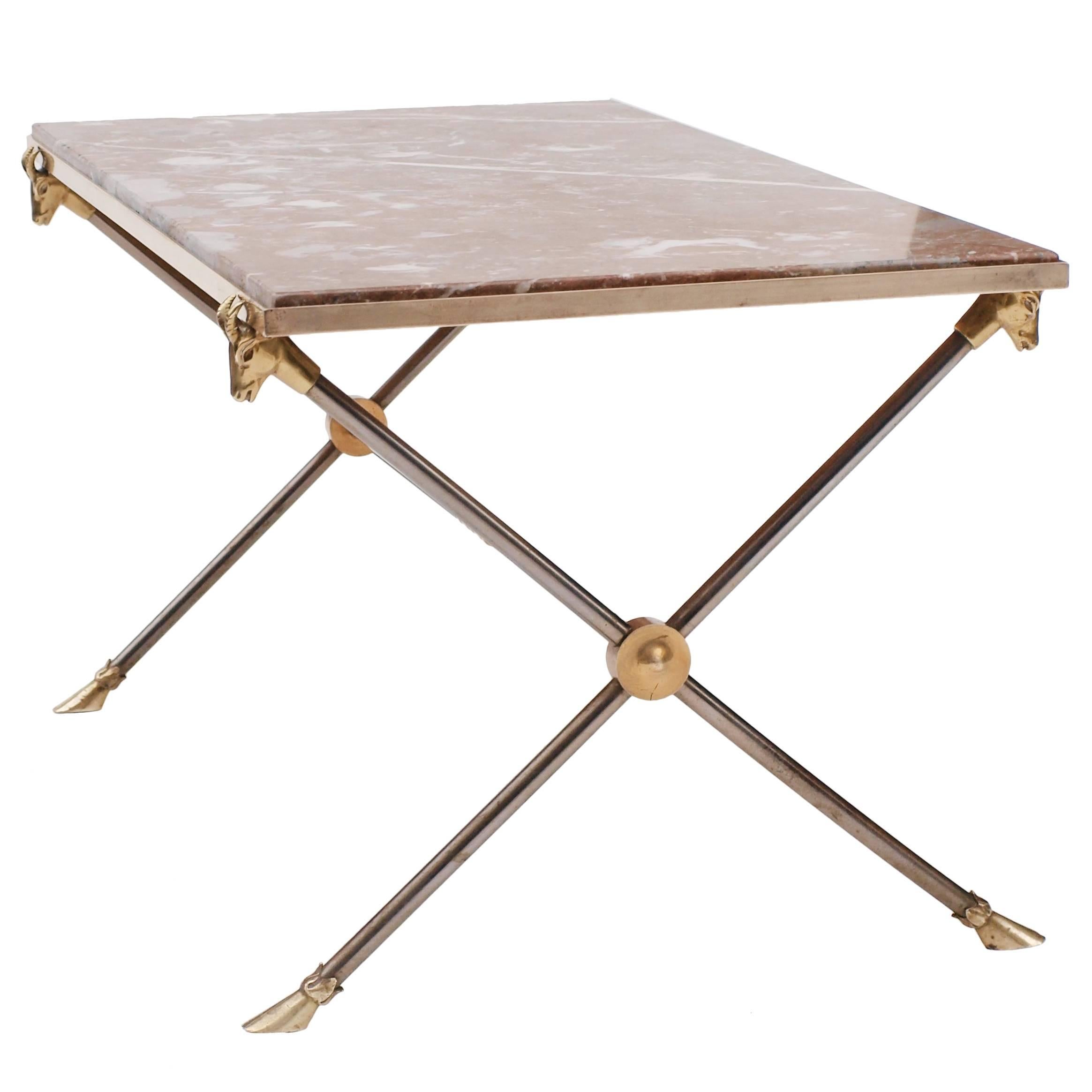 A Maison Ramsay coffee table in brass and nickel, ram's head details supporting the richly colored marble top and hoof shaped feet.
  
