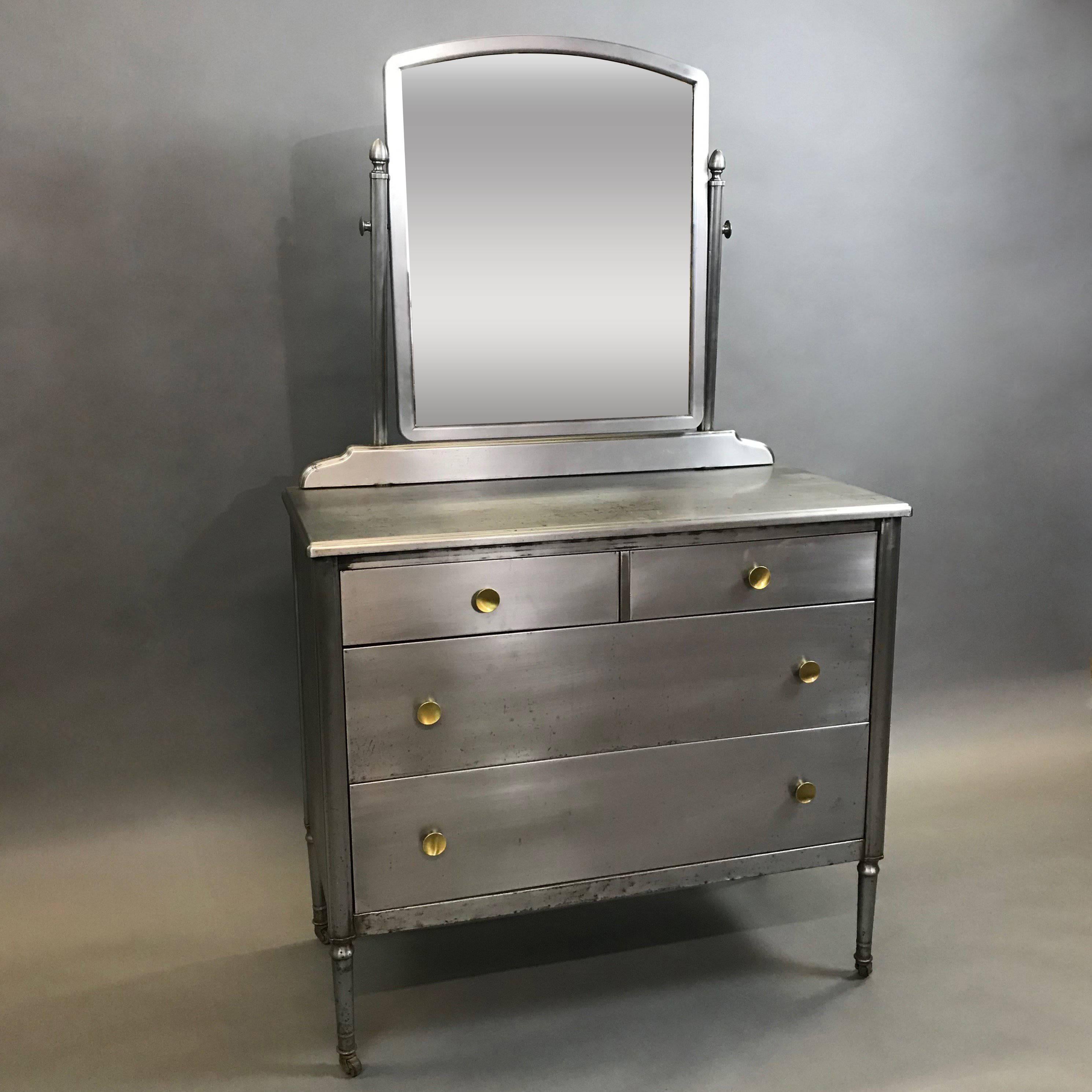 Wonderfully detailed, Sheraton series, pressed steel dresser with original tilt adjustable mirror by Simmons Furniture Company features drawers with brass pulls, interior blue paint on rolling casters.

Dresser dimensions are 40in W x 19in D x