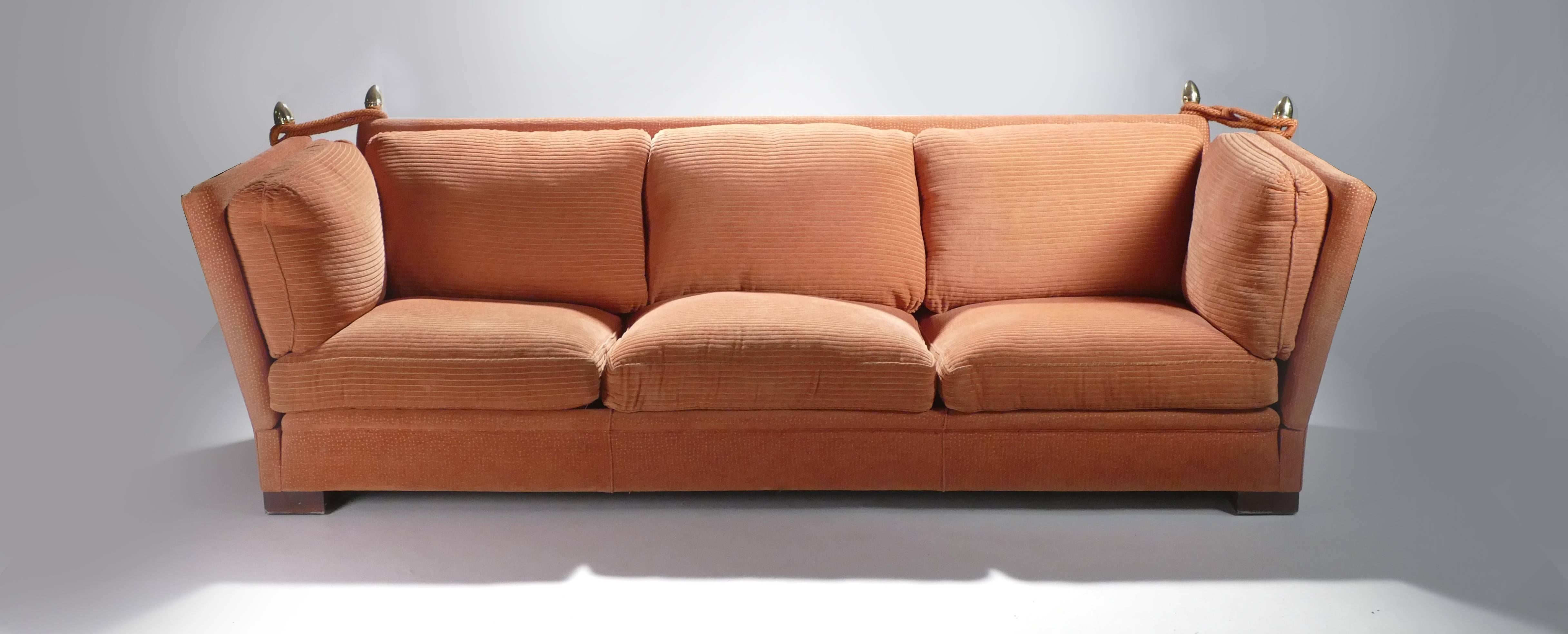 The burnt orange fabric of this pair of Mid-Century Modern sofas is the original 1970s upholstery and has been maintained in very good vintage condition. With inventive, extendable armrests at either side and thick, plush cushions, these sofas are