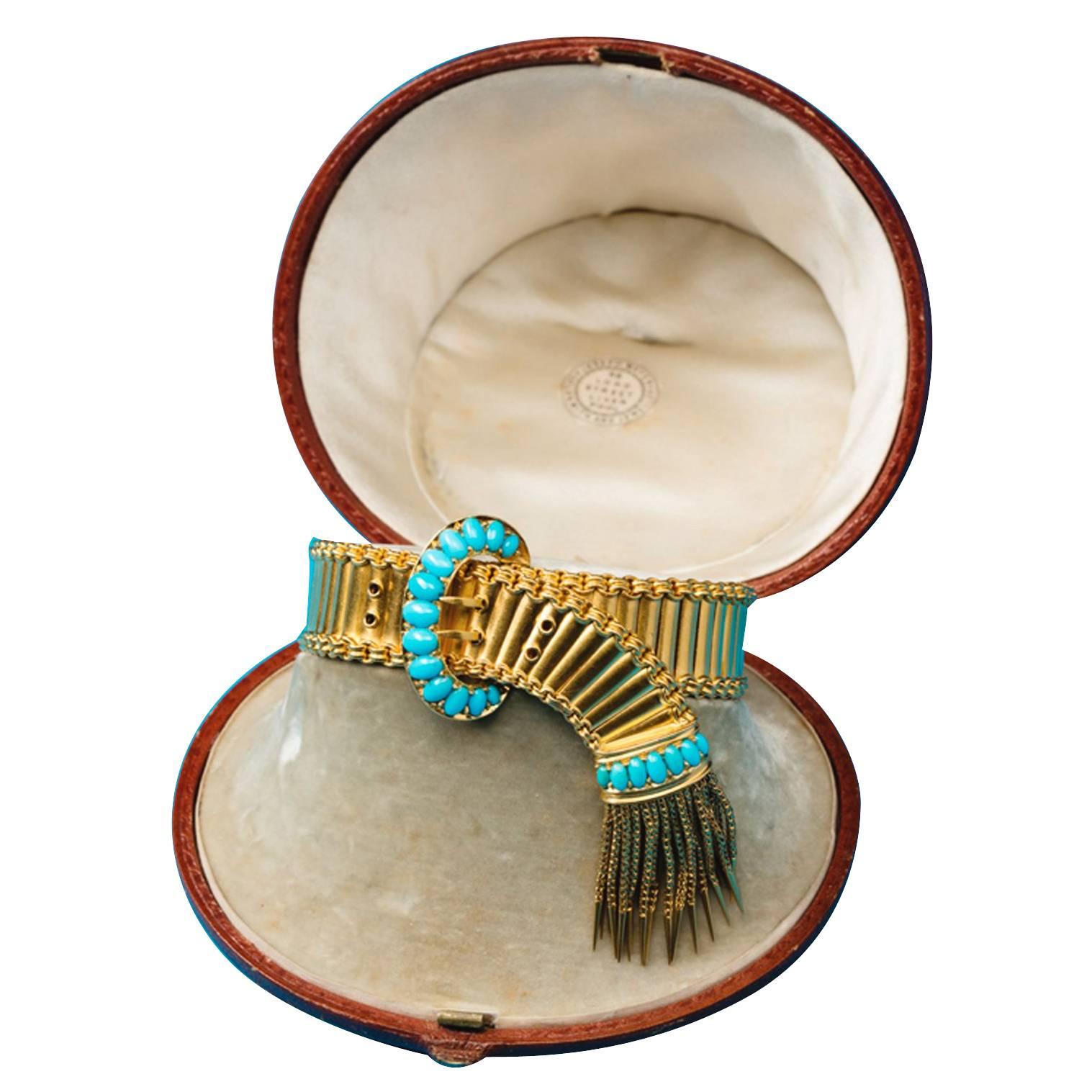 An 18-carat gold buckle bracelet, the central buckle is set with graduated cabochon cut turquoises, the end has a band of turquoises and a gold tassel, England, circa 1870, in its original case.

weight: 47.3 grams
length: 18.5 cm