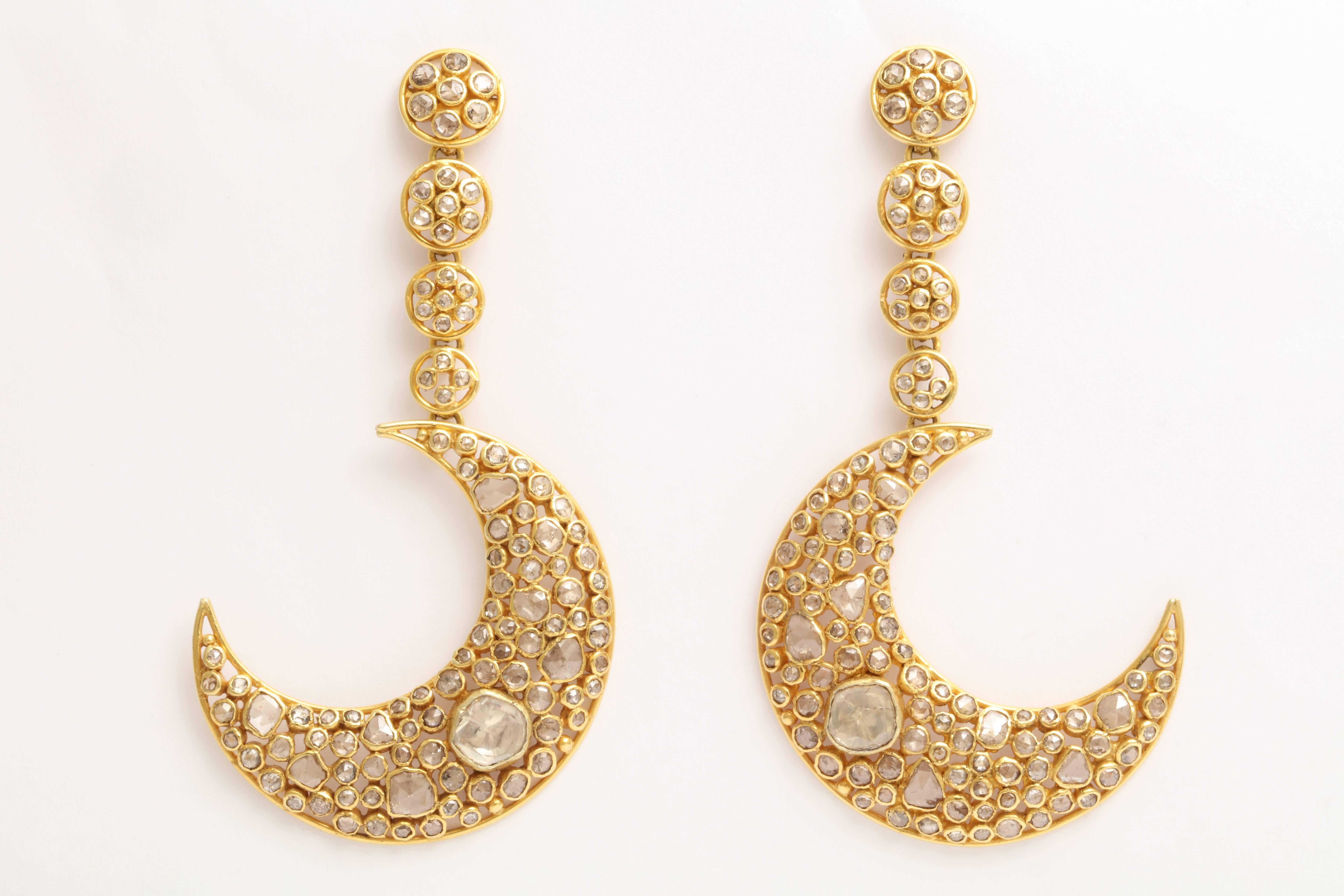 A pair of 18kt yellow gold and diamond moon earrings. The moons are suspended from graduated 18kt yellow gold and diamond set discs. The moons and discs are filled with bezel set rose cut diamonds and polki diamonds.
The approximate diamond weight