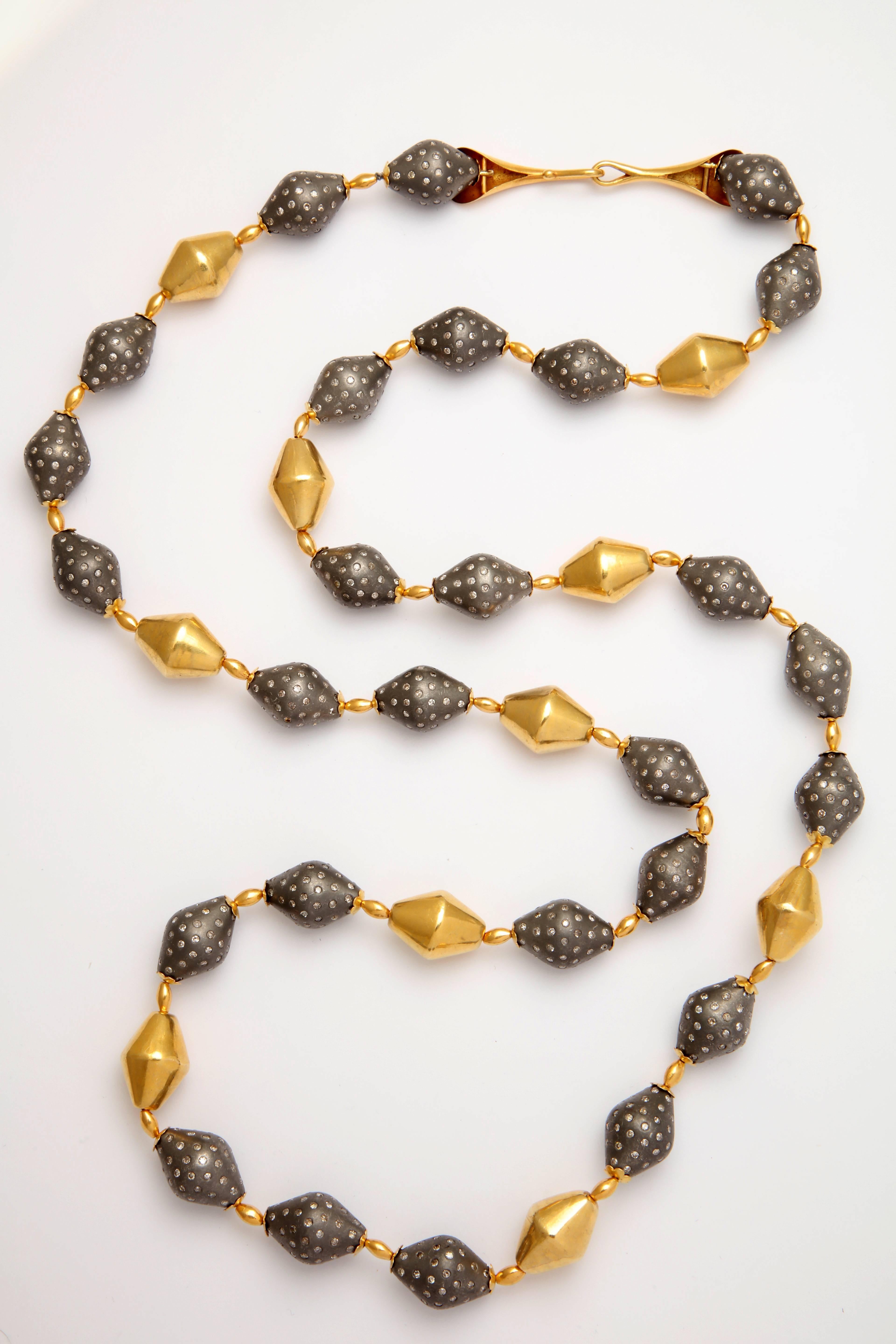 A necklace composed of 18kt yellow gold beads and rhodium plated sterling silver beads set with diamonds. There are 18kt yellow gold flower caps on either end of the silver beads. The 18kt yellow gold trumpet clasp measures 2.50 inches long. There