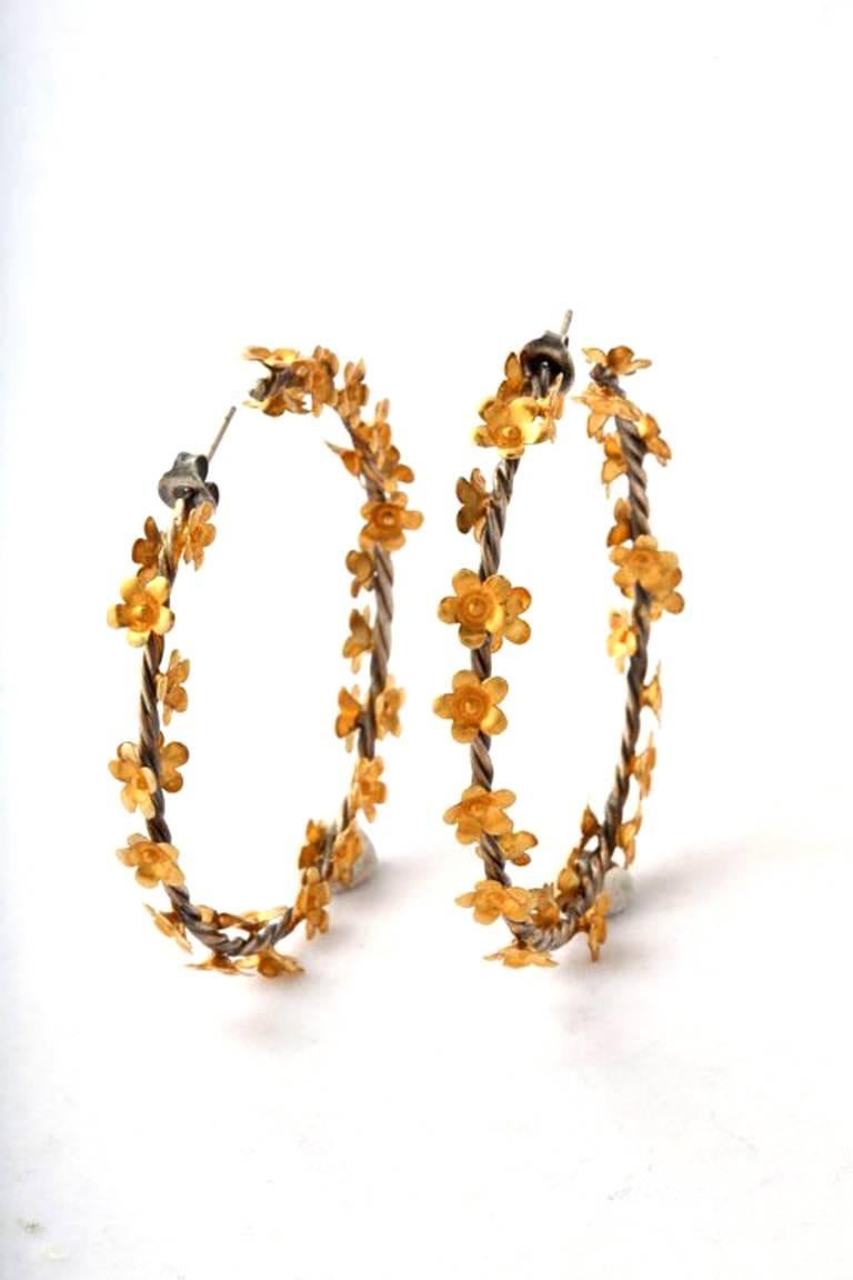 A pair of rhodium plated sterling silver twisted vine hoop earrings with scattered 18kt yellow gold flowers.
Width: 2 inches
