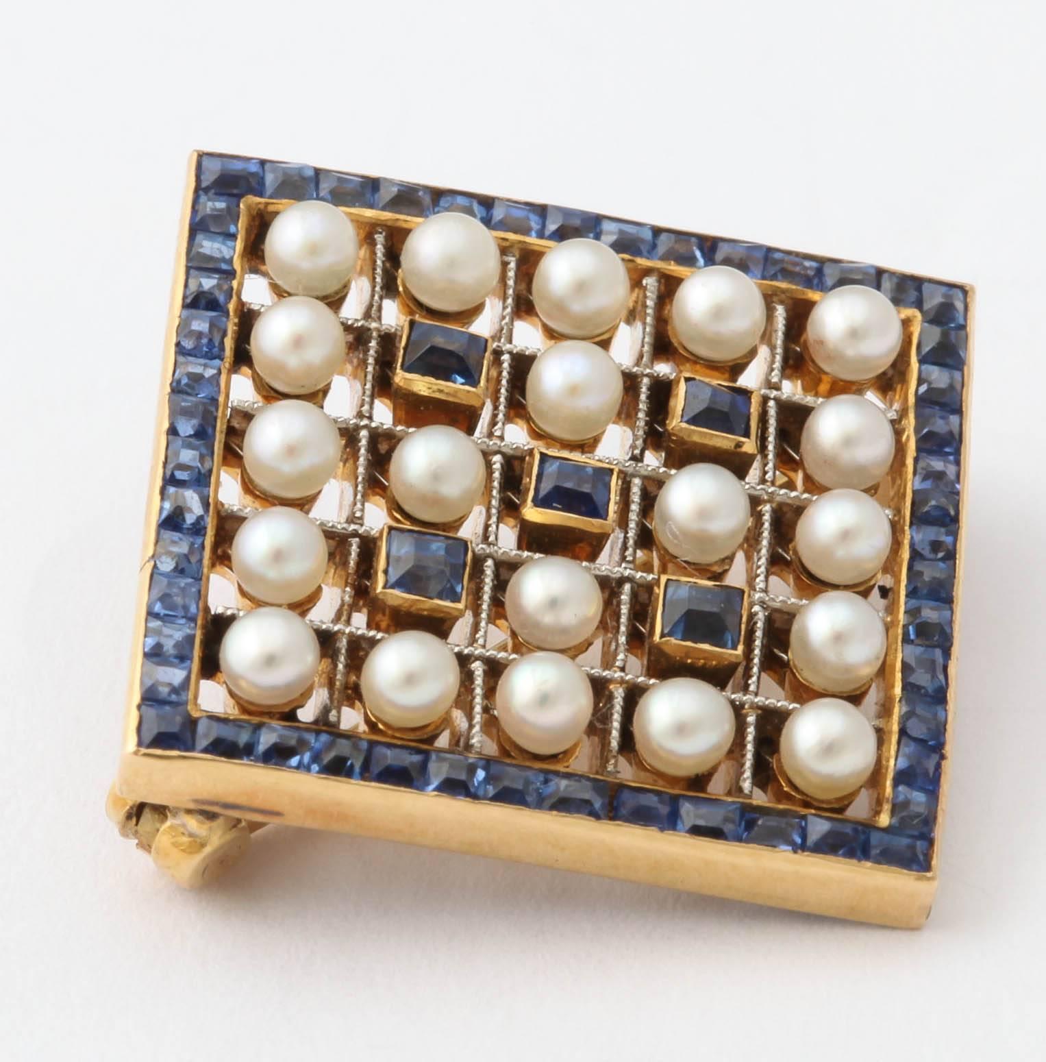 An exquisite diamond-shaped pin forming an openwork 18k gold lattice set with alternating square-cut sapphires and small lustrous pearls. The border is channel-set with square-cut sapphires. In its original fitted case stamped D. J. Wellby Ltd.,