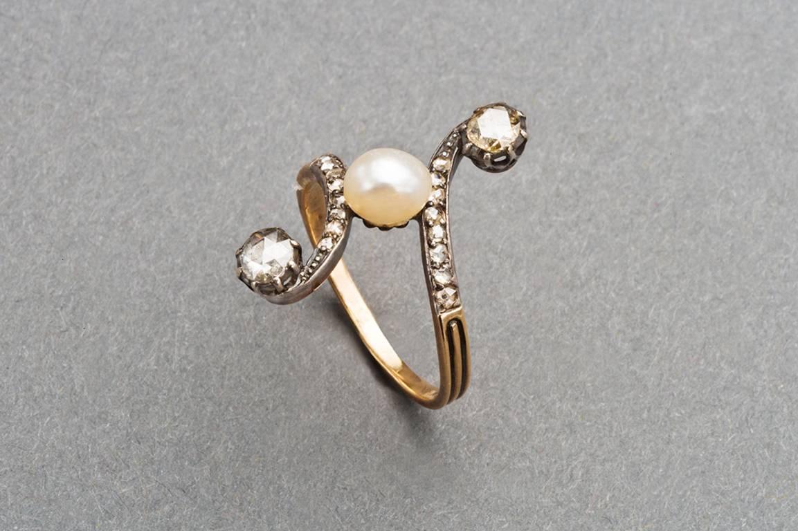 A French scrolling diamond and pearl ring of rococo design set with an oval pearl, the curved shoulders enhanced with lines of rose diamonds, each ending in an oval rose diamond, mounted in silver and 18k rose gold.

Circa 1890, unmarked except for