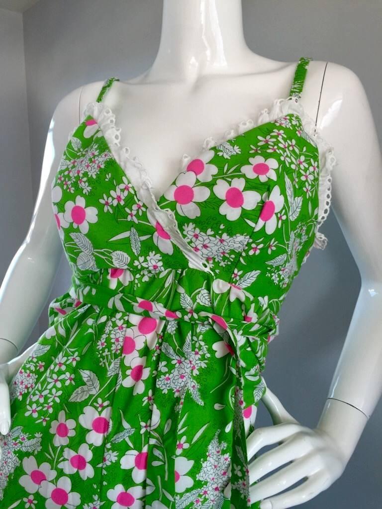 Incroyable combinaison en coton vintage des années 70 ! Couleur vert fluo, avec des fleurs roses et blanches sur toute la surface. Le buste est garni d'une adorable dentelle blanche à œillets. Pantalon à jambe large. Ceinture à nouer à la taille,