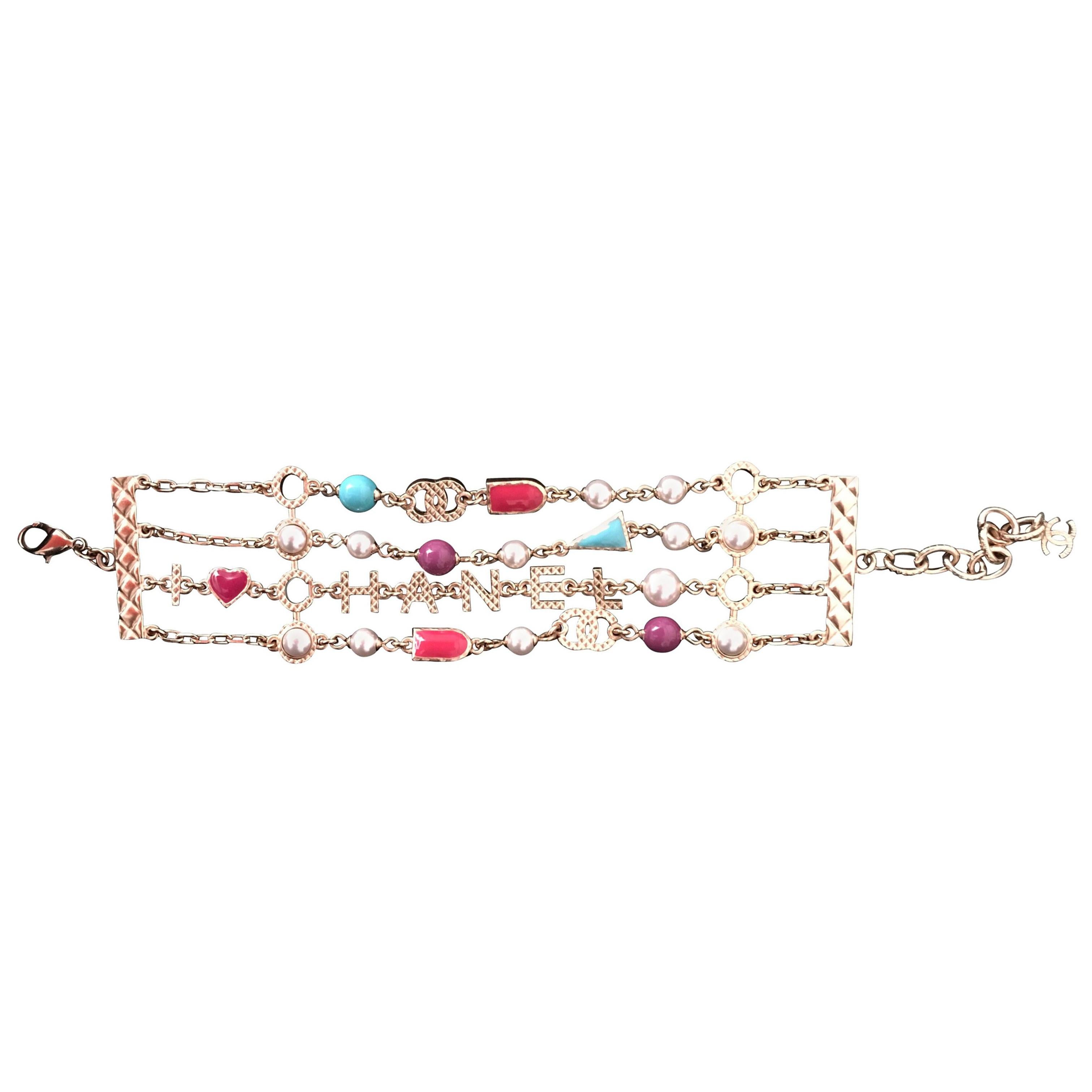 Presented here is a brand new Chanel bracelet with pearls Multi colored stones and Chanel written out one of the four chains which encompass the beautiful bracelet. The gold tone piece has four rows of very typical Chanel classic style., with white