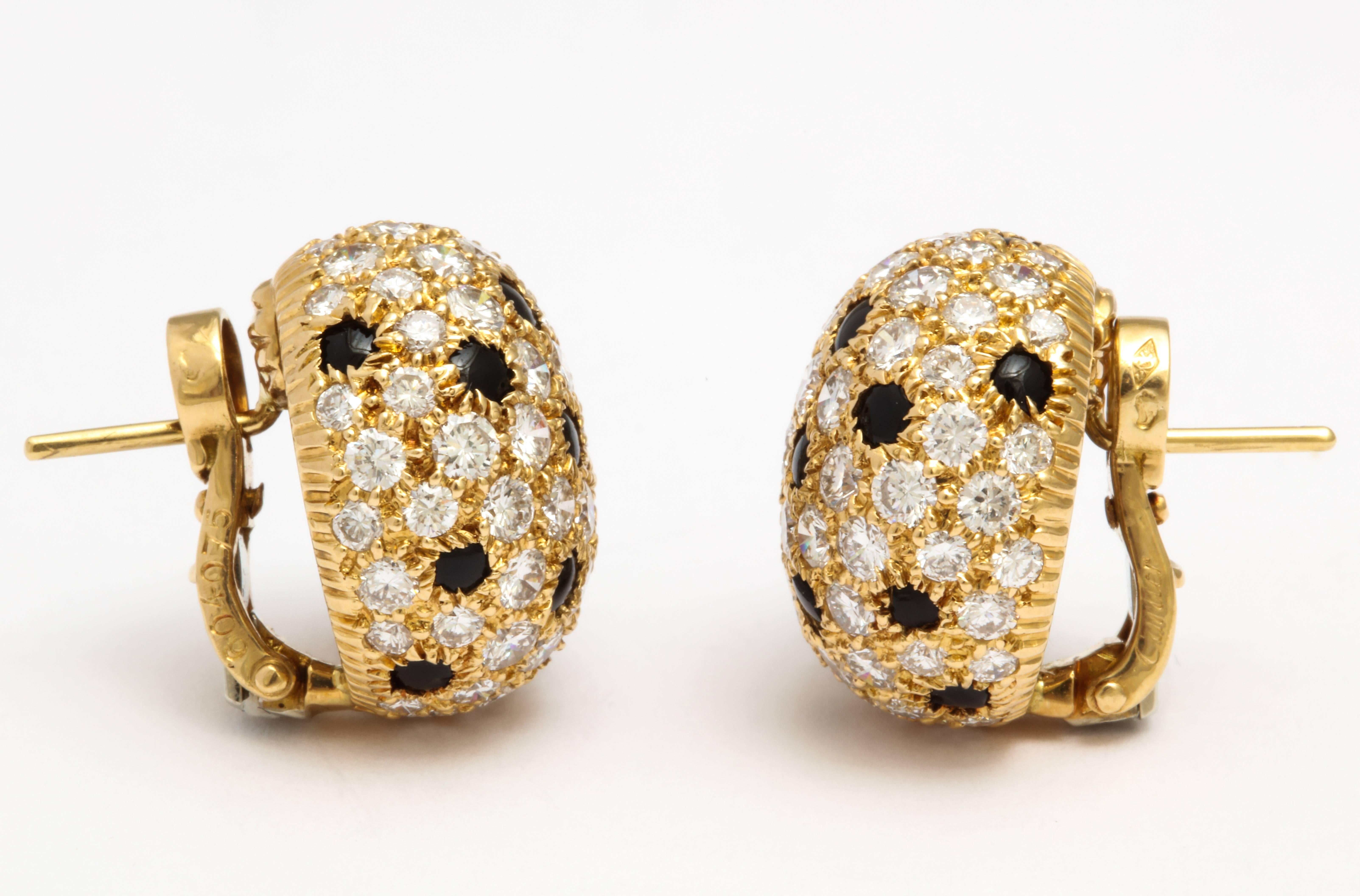 A pair of earrings by Cartier set in 18 karat yellow gold. Each bombé circular cluster has pavé-set brilliant-cut diamonds with a total weight of approximately 6 carats, and is interspersed by buff-top onyx spot detail. French marks. 

Signed