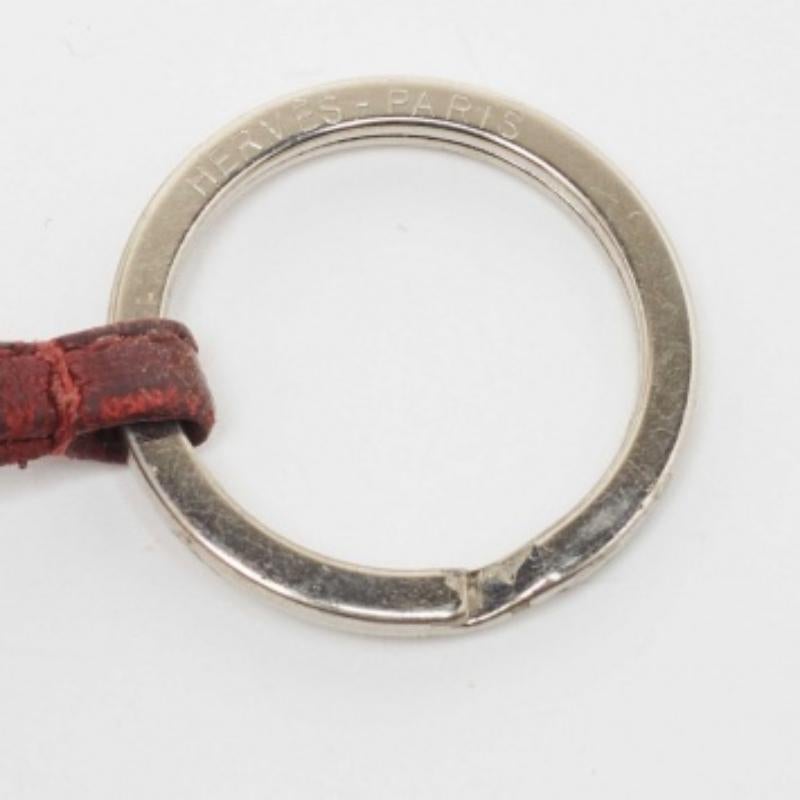 Questo elegante portachiavi proviene dalla casa di Hermes. Il portachiavi è dotato di una nappina in pelle color rubino e di un anello con incisione dell'etichetta.