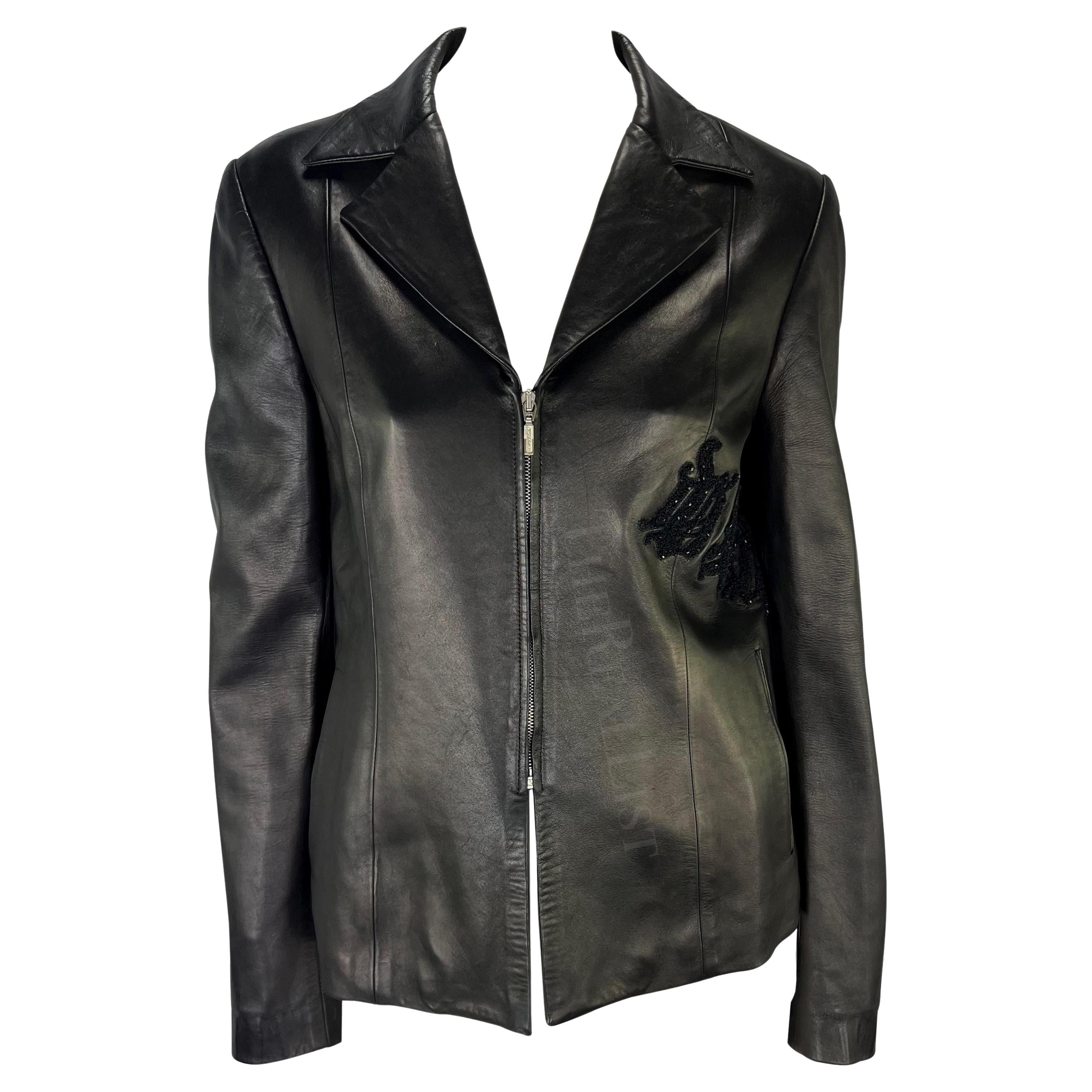 Ti presentiamo una giacca di pelle nera di Gianni Versace, disegnata da Donatella Versace. Questa giacca della collezione Autunno/Inverno 1999 è realizzata interamente in pelle e presenta un colletto ripiegato e una chiusura a zip. La giacca è