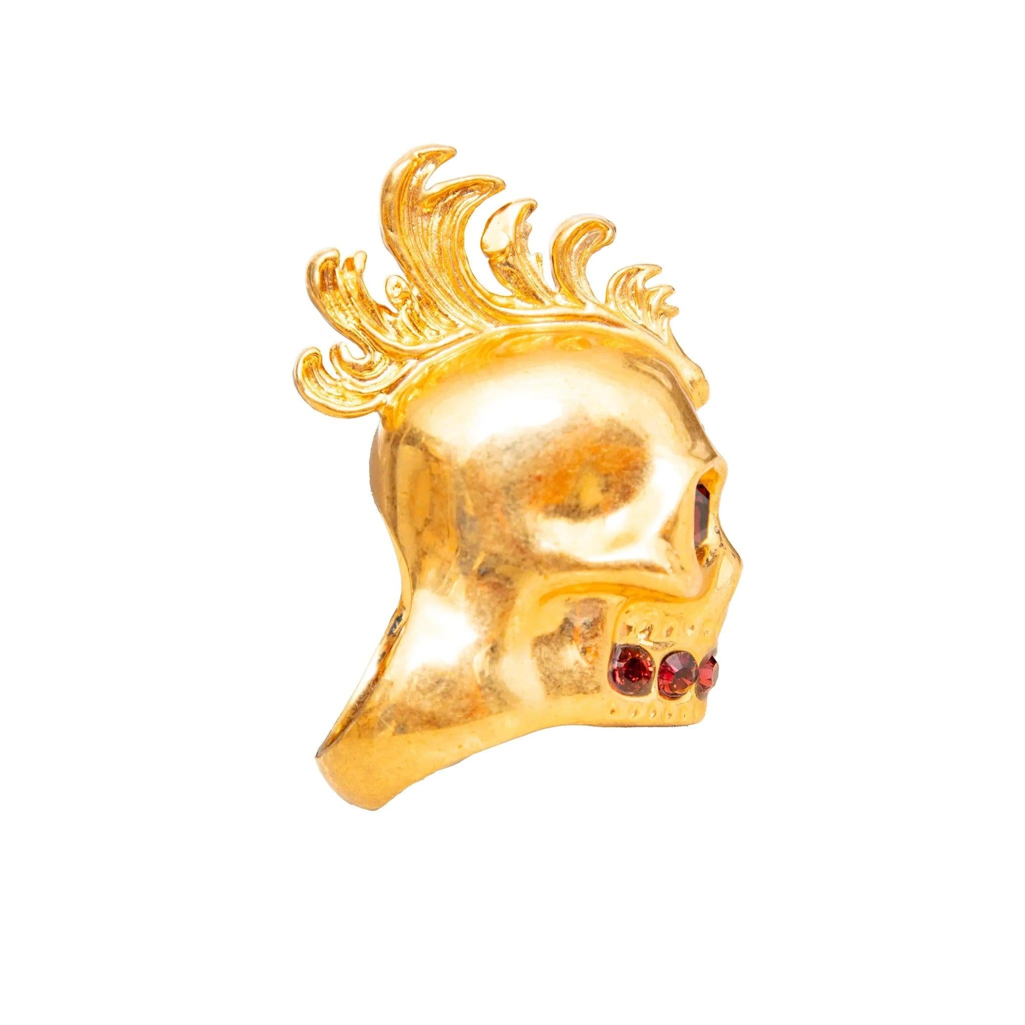 Anello con teschio di Alexander McQueen in metallo placcato oro, con pietre rosse e un audace disegno di teschio con mohawk. Un'affermazione di lusso e di tendenza.
 Inclusione: scatola. 
 Osservazioni: Le dimensioni e il materiale non sono