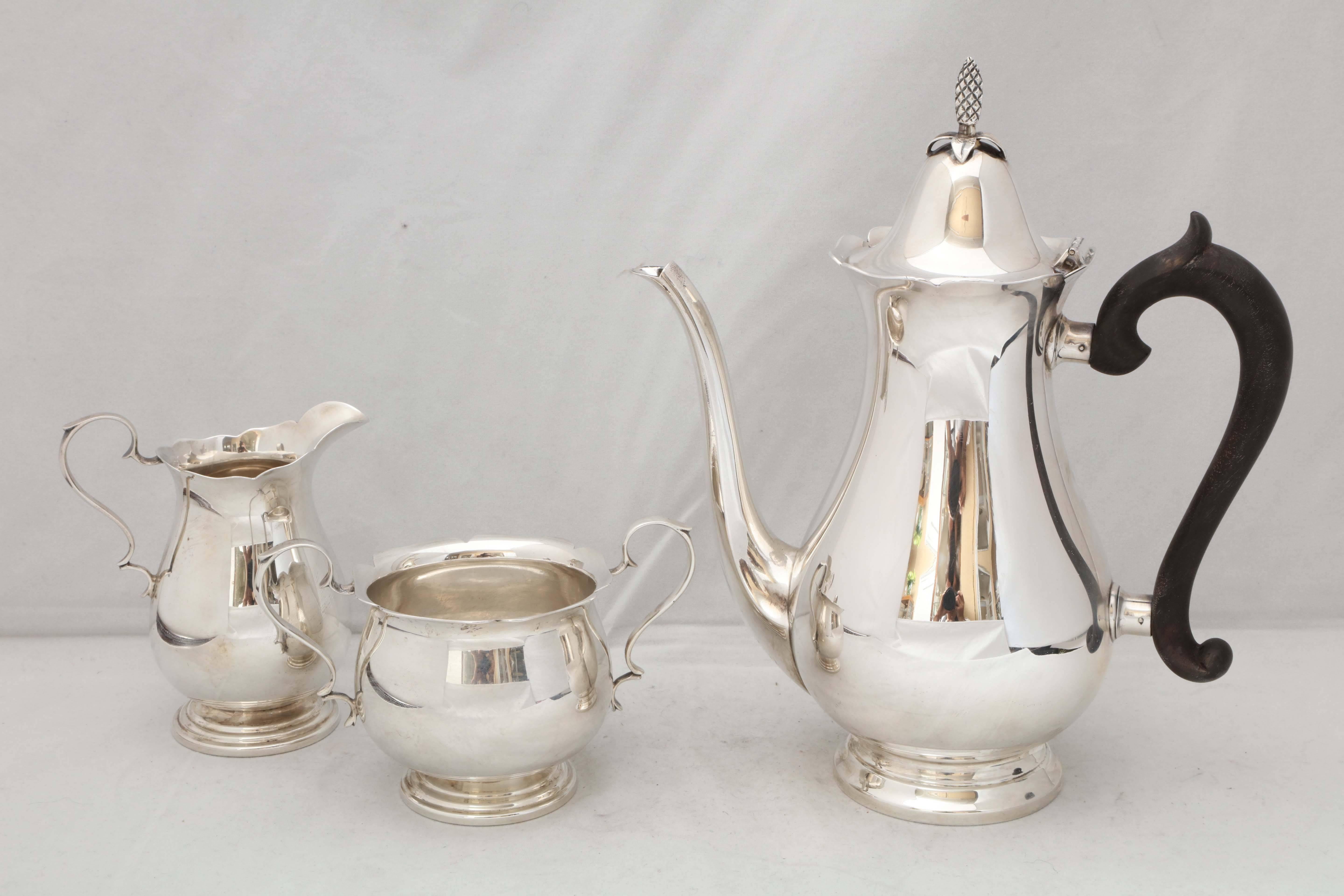 Sterling silver, American Colonial style, three-piece coffee or tea set, Genova Silver Co., New York, circa 1950s. Coffee or tea pot has a wooden handle and is topped by a pineapple finial (a symbol of 