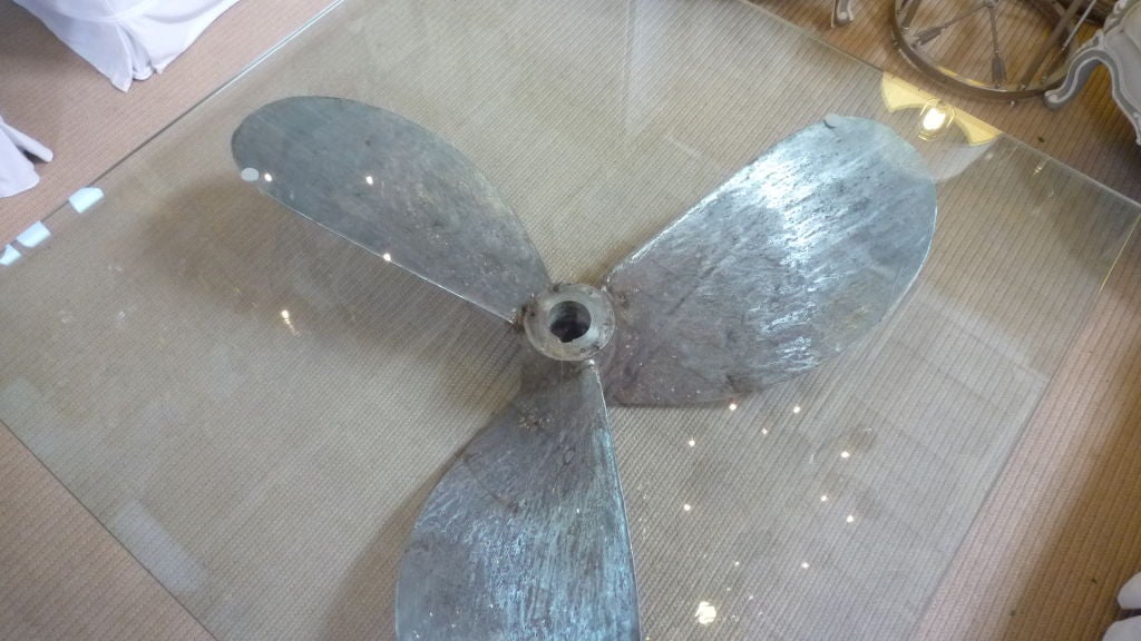 An old Cast iron ship's propeller made into a coffee table. A thick square glass top as the table top.