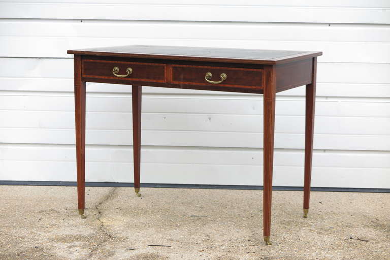 English leather top desk on tapered legs with brass casters. Nice banding detail on front and legs.