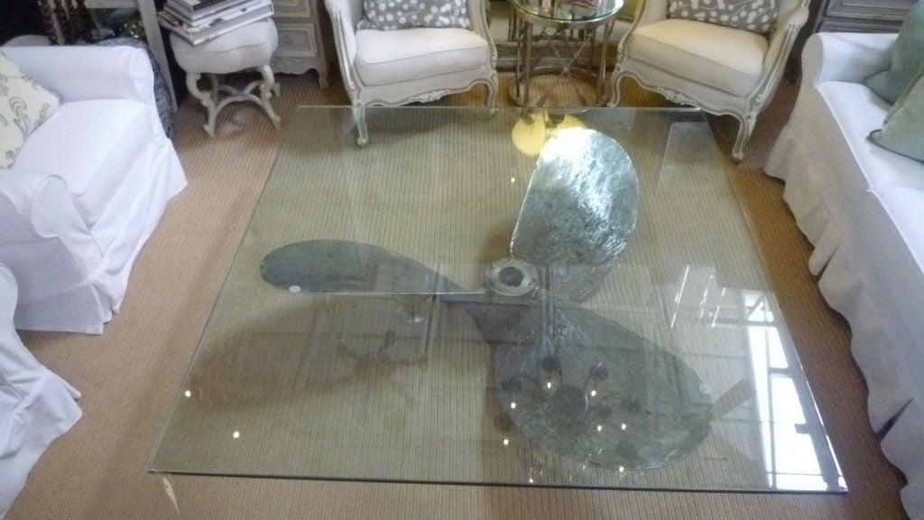 This unique coffee table is made from an old ship's propeller, using a square glass panel for the table top.